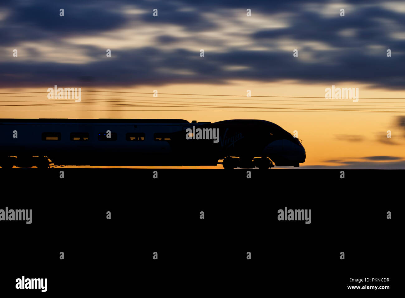 Ein Virgin Trains Westküste Pendolino train eine Silhouette bei Sonnenuntergang auf der West Coast Main Line und Geschwindigkeit. Stockfoto