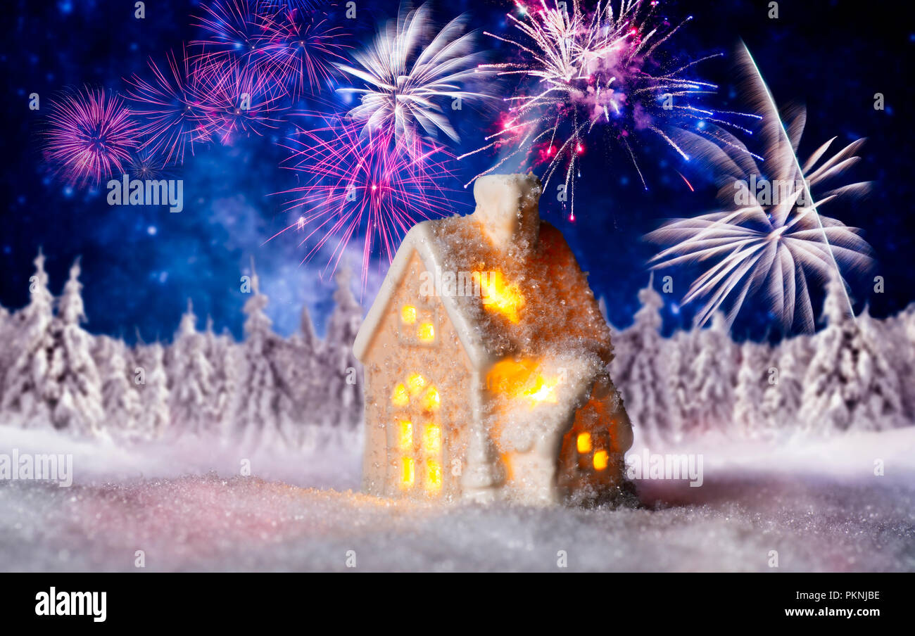 Kleines Beleuchtetes Haus mit Winterlandschaft und Feuerwerk im Hintergrund Stockfoto