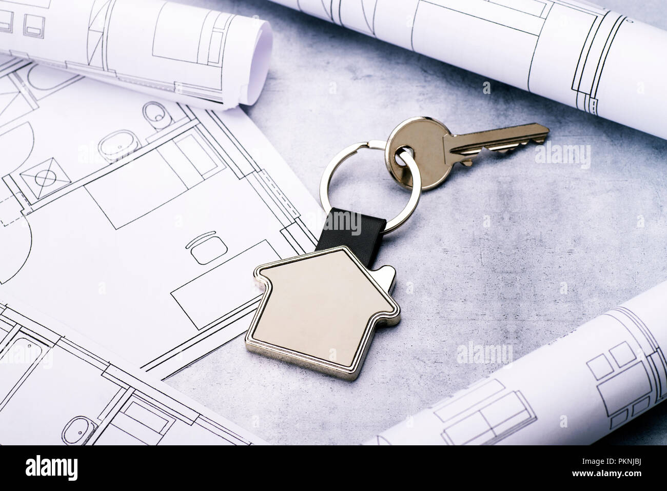 Schlüssel mit Haus als Schlüsselanhänger und Blueprints auf einen konkreten Hintergrund Stockfoto