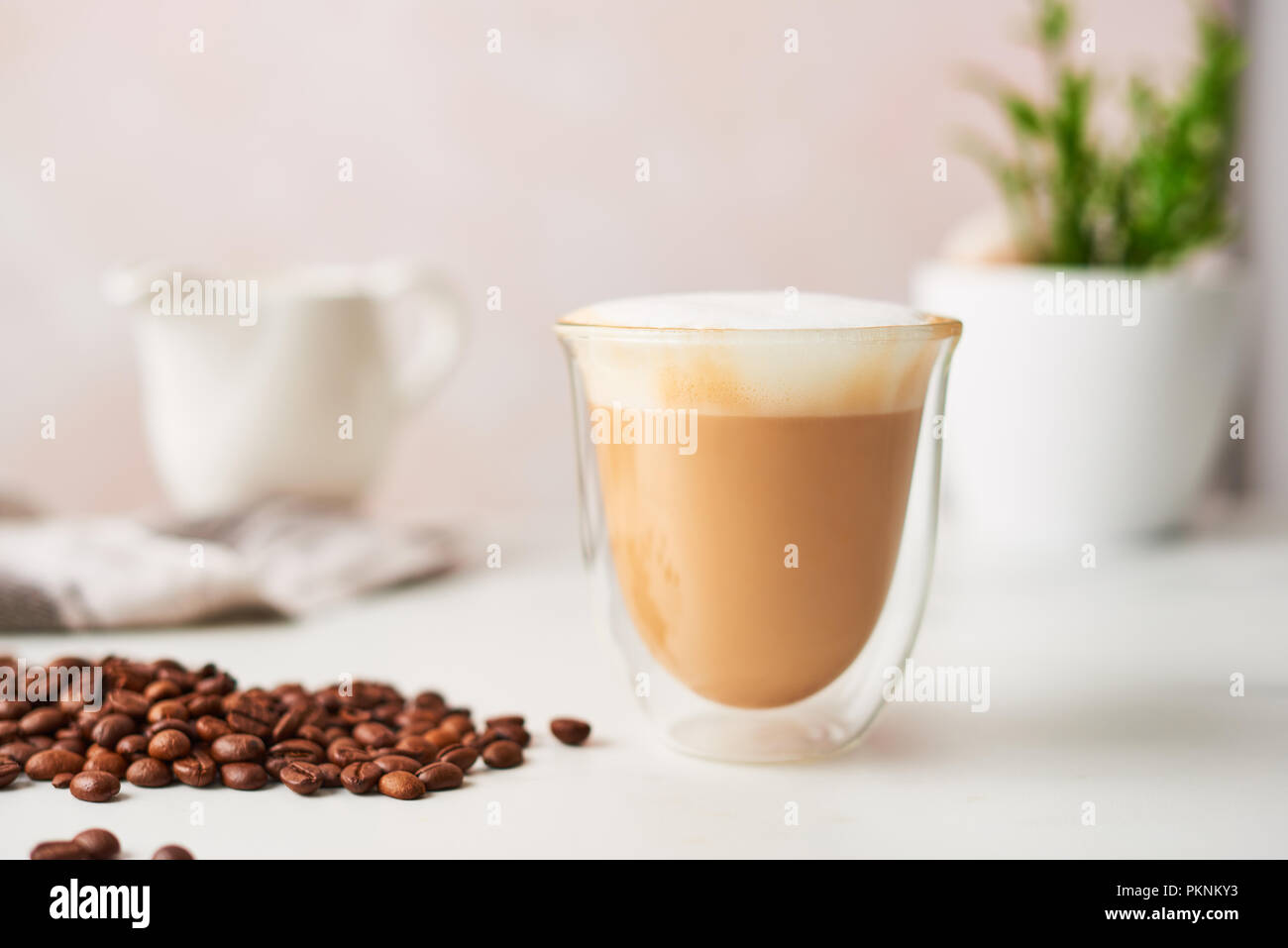 Cappuccino in einem doppelwandigen Glas mit gerösteten Kaffeebohnen. Feminine rose Hintergrund mit kopieren. Bild mit hoher Auflösung, enge Tiefenschärfe. Stockfoto