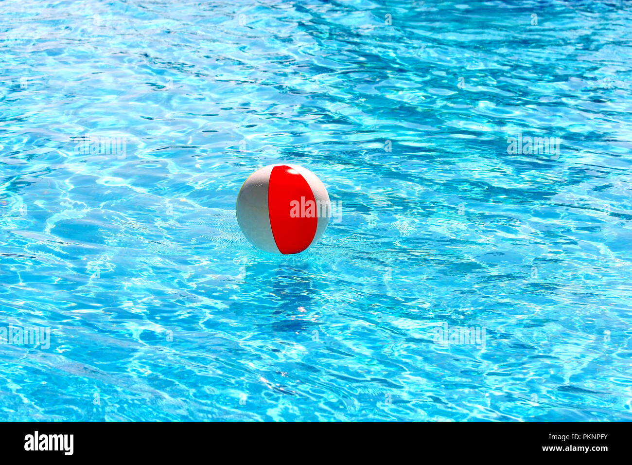 Beach ball Floating in einem Pool mit kleinen Wellen im Sommer Sonne widerspiegelt Stockfoto