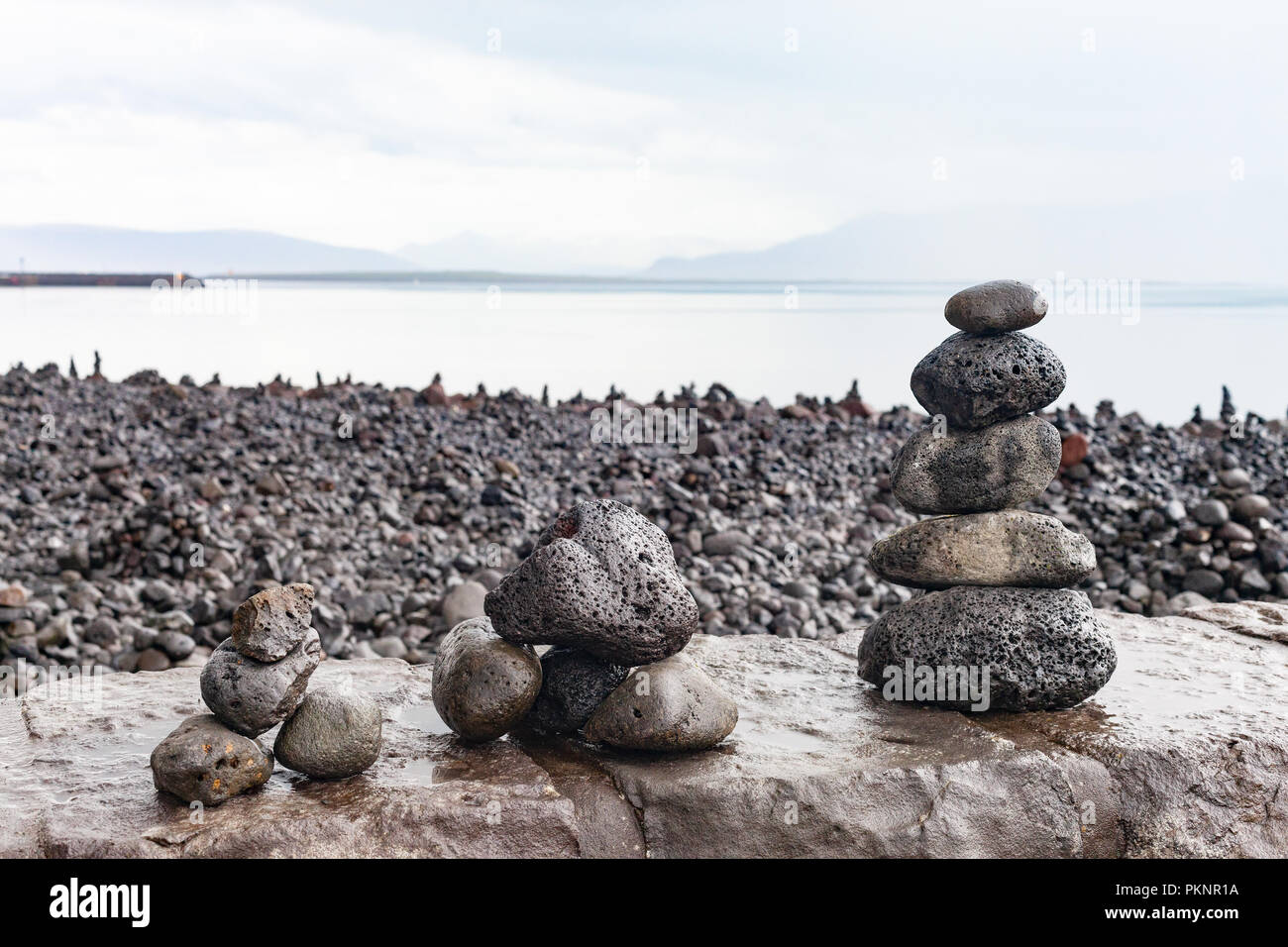 Zen - wie Cairns aus Lavagestein von Touristen gebaut auf der Uferpromenade in Reykjavik, mit Blick über die Bucht von Faxa auf die Halbinsel Snaefellsnes, Island Stockfoto