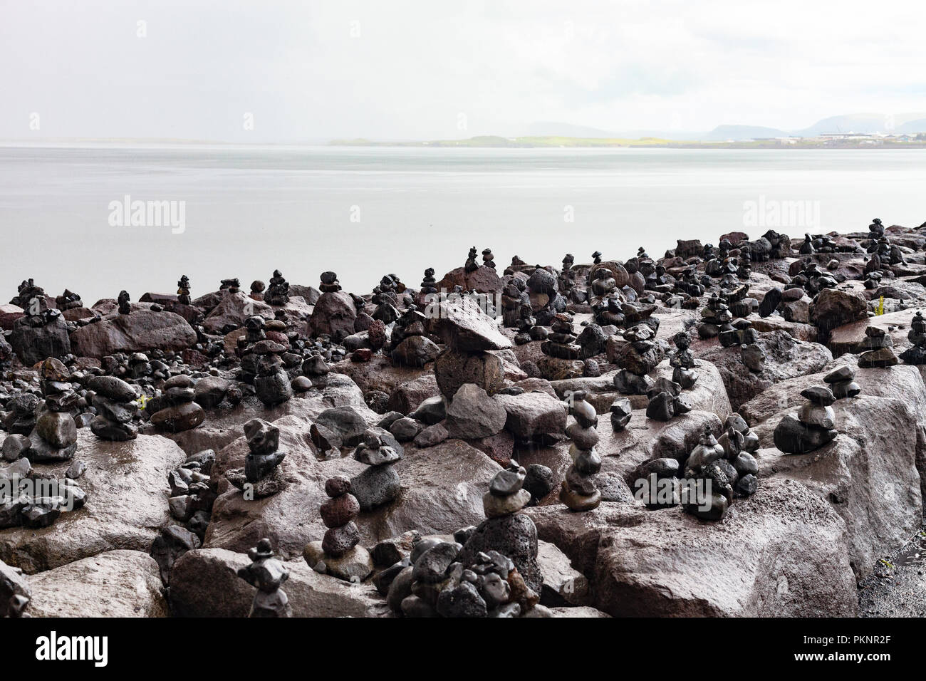 Zen - wie Cairns aus Lavagestein von Touristen gebaut auf der Uferpromenade in Reykjavik, mit Blick über die Bucht von Faxa auf die Halbinsel Snaefellsnes, Island Stockfoto