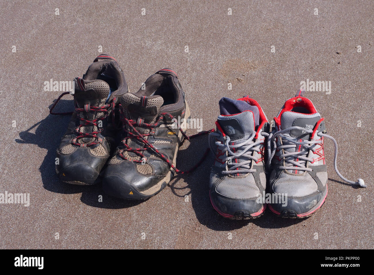 Zwei Paare von verschlissenen Walking Trainer auf dem Sand links, während die Eigentümer einen Tag am Strand geniessen Stockfoto