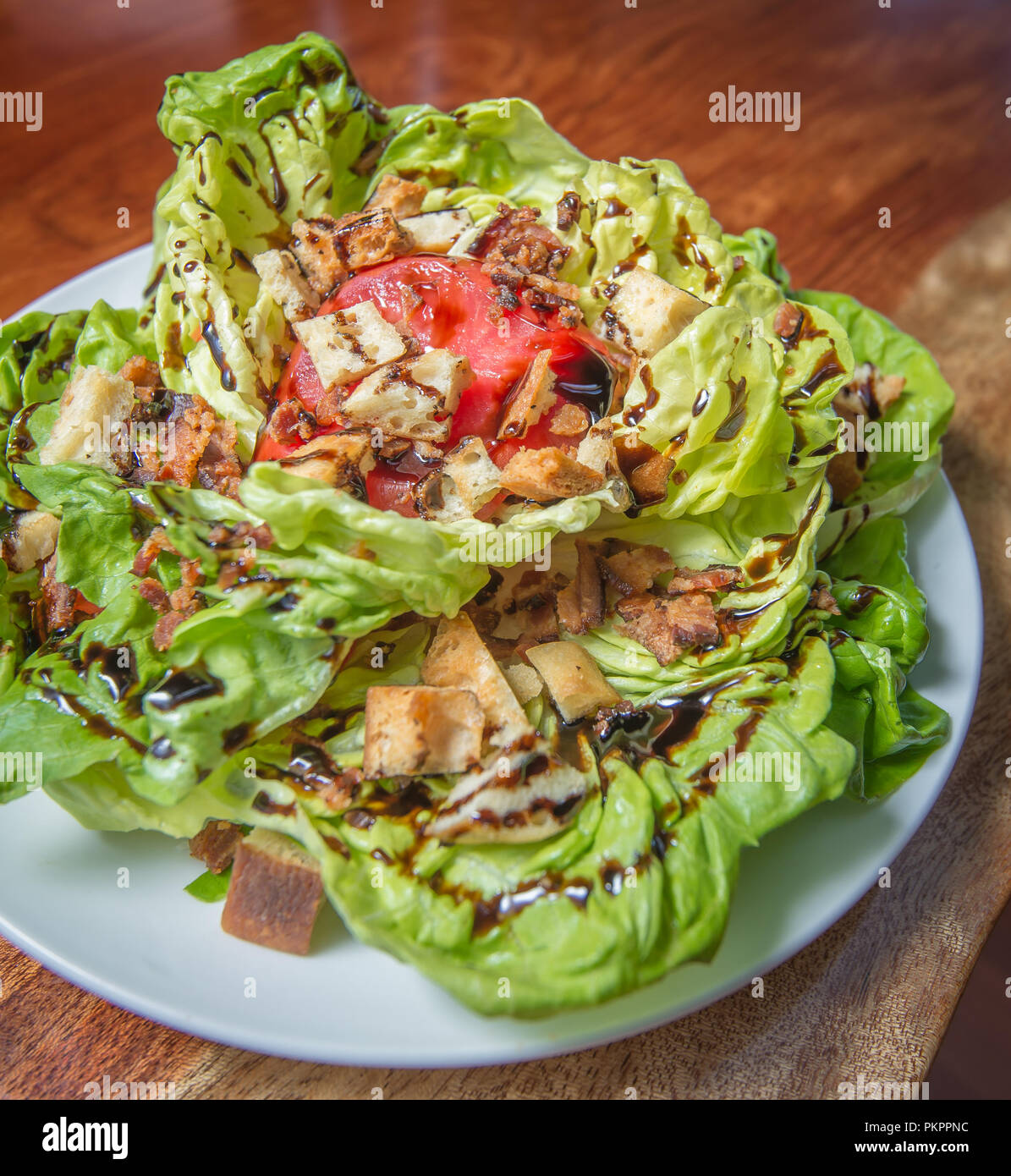 Ein BLT Salat mit Speck, Tomaten und Croutons auf einem Holztisch Stockfoto