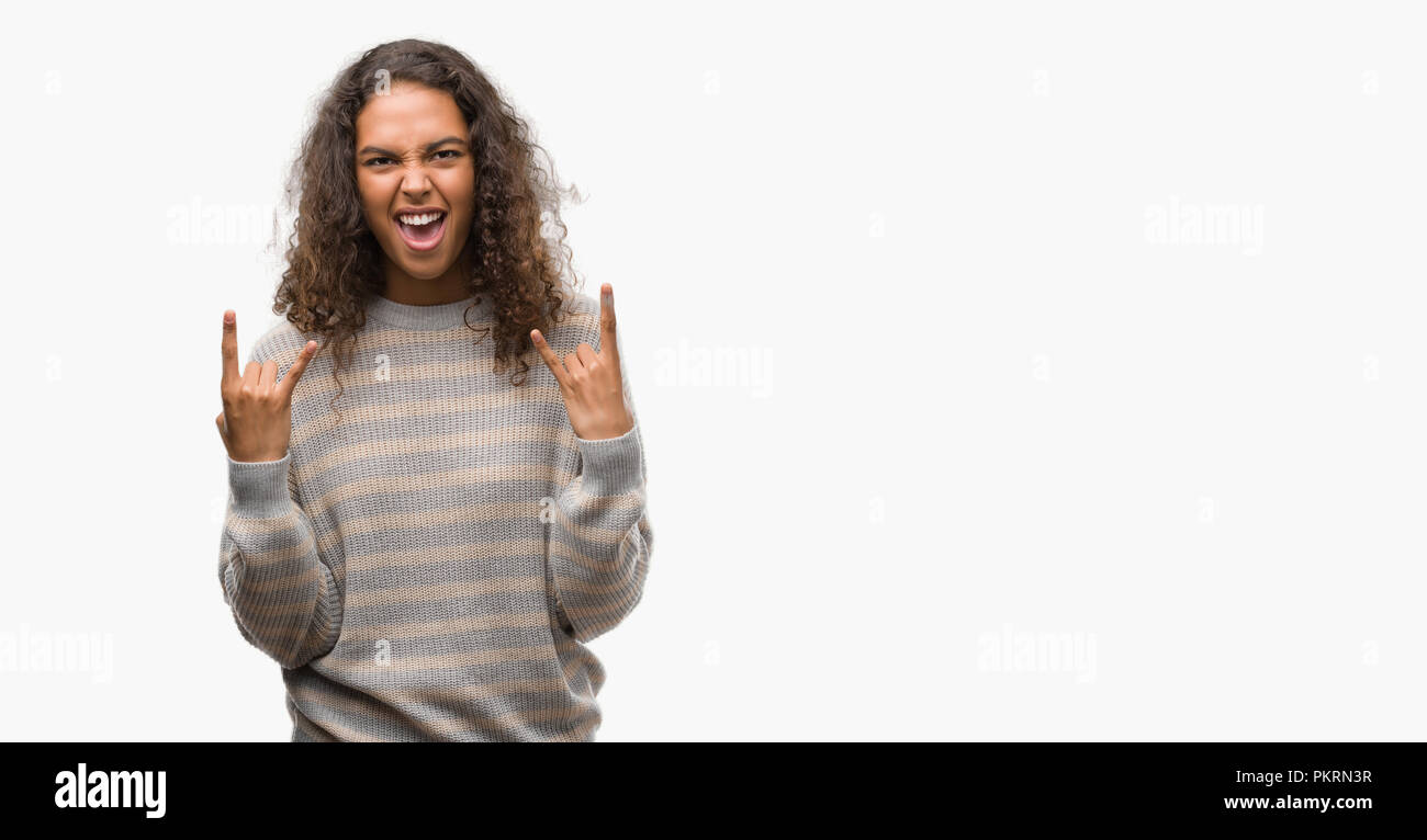 Schöne junge Hispanic Frau tragen Streifen Pullover schreien mit verrückten Ausdruck tun Rock Symbol mit hands up. Musik Star. Schwere Konzept. Stockfoto