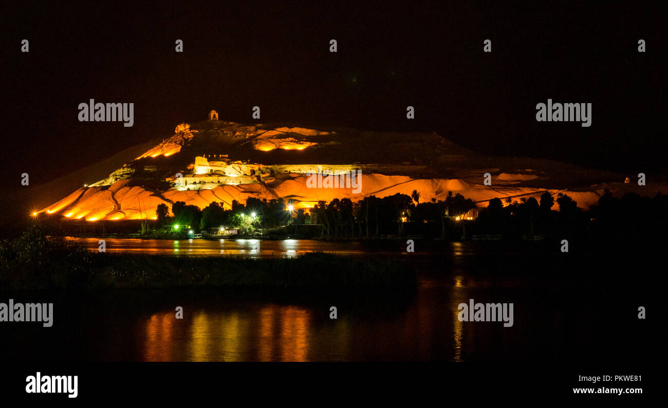 Nacht Blick über den Nil mit lichtreflexionen Qubbet el-Hawa Grab zu Hügel, Kuppel der Winde, und alten Hügel Gräber, Assuan, Ägypten, Afrika Stockfoto