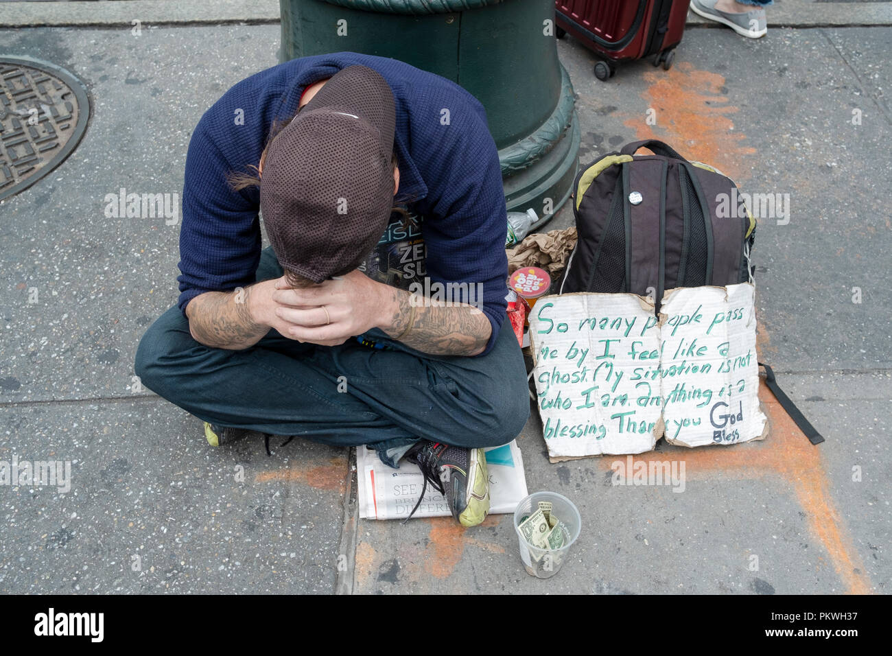 Ein zerknirschter junger Mann an der 42nd Street und Sixth Avenue mit einem Schild um Spenden mit einer bewegenden Schild, er ist nicht unsichtbar. Stockfoto