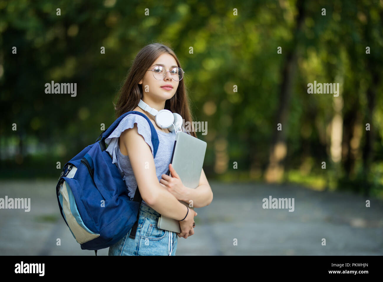 Freundliche attraktive Frau mit Rucksack und Notebooks stehen und lächelte in Park Stockfoto