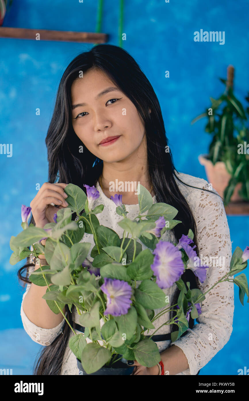 Mädchen, dass ein Topf von Violett petunie vor einem blauen Hintergrund. Stockfoto