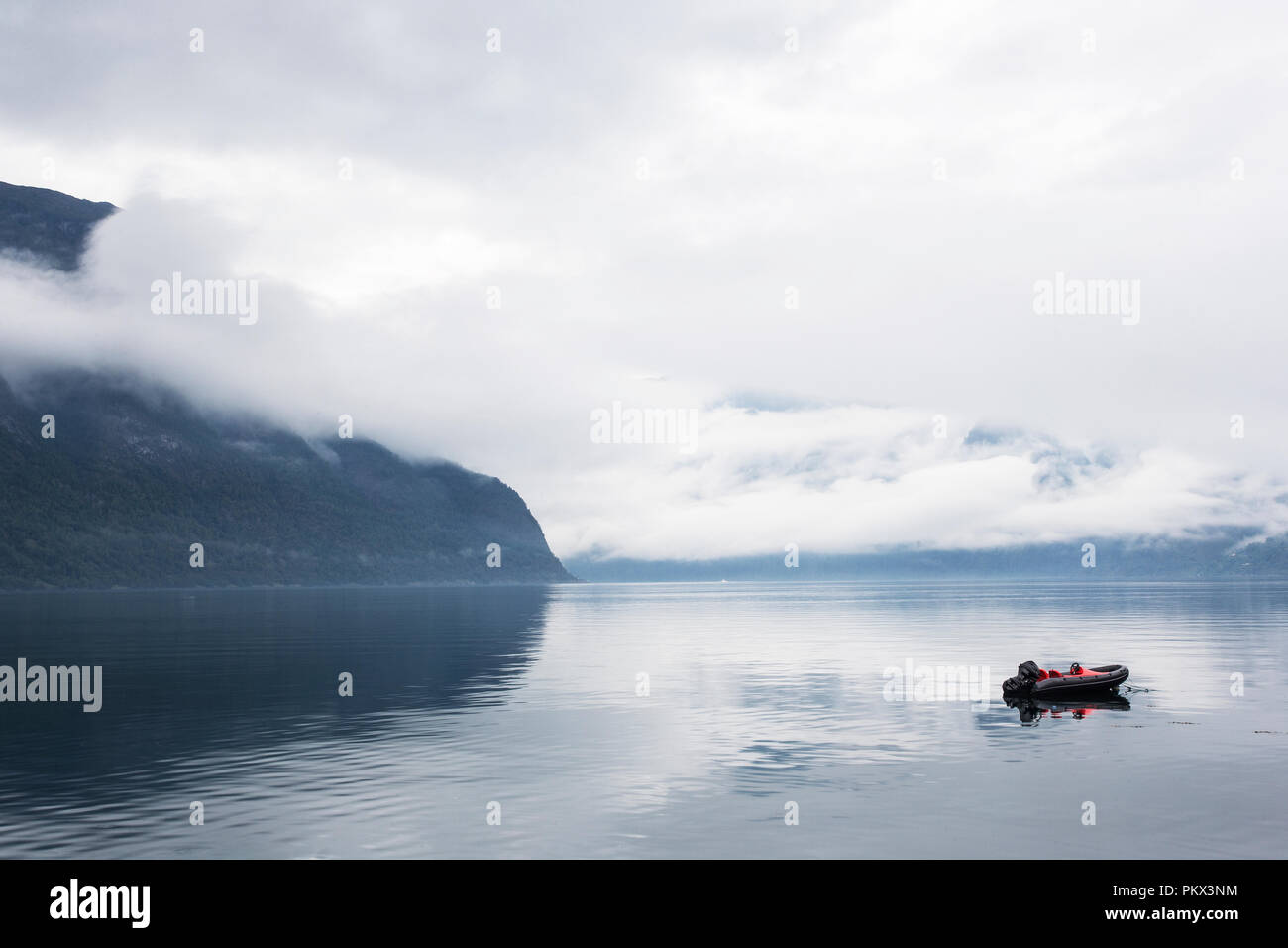 Kleines Boot an einem nebligen ruhigen See mit Bergen im Hintergrund Stockfoto