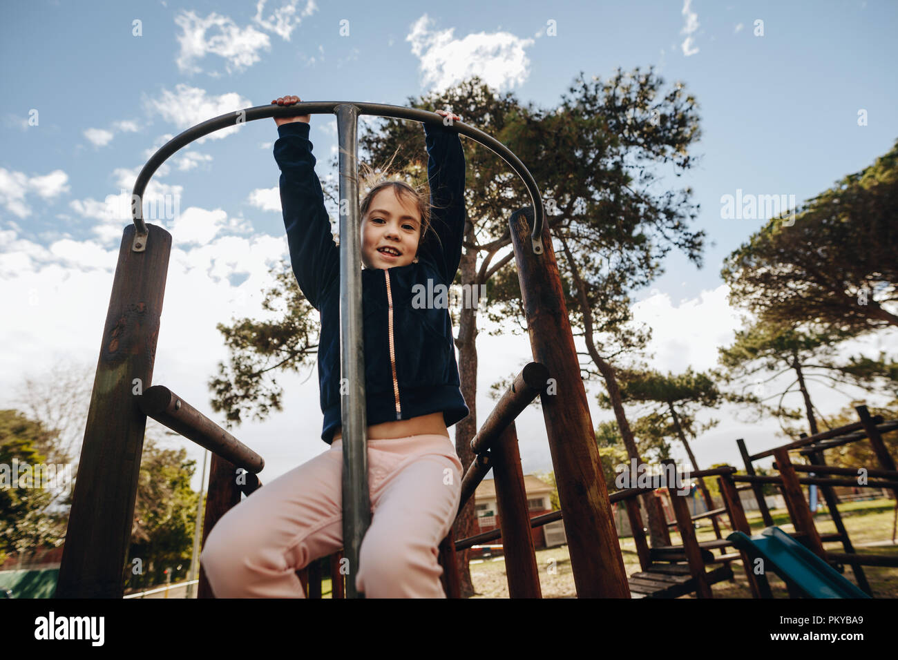 Porträt eines jungen Mädchens hängen an einem Klettergerüst durch ihre Arme. Kleine Mädchen spielen in den Spielplatz. Stockfoto
