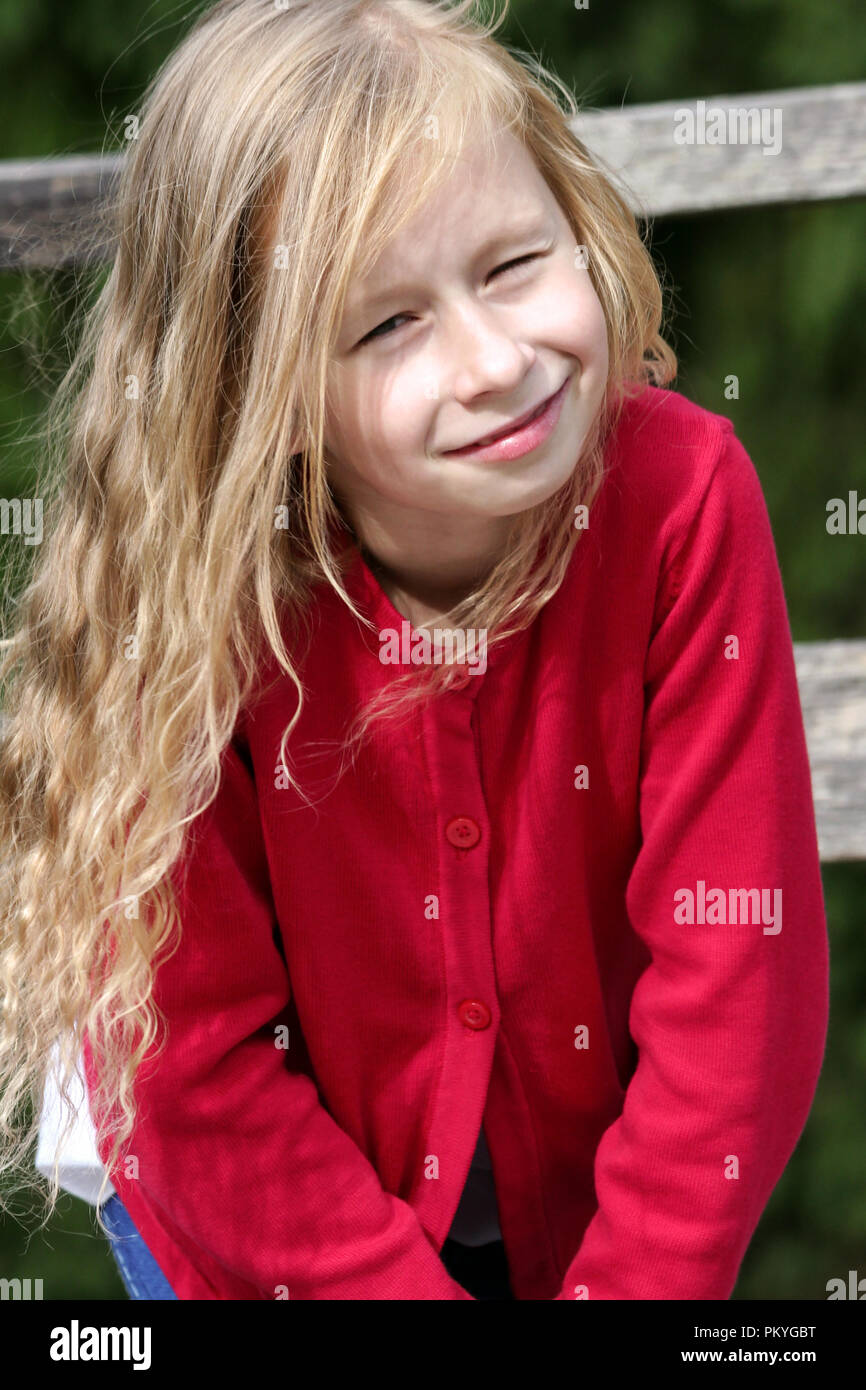Kleine Blonde Madchen Mit Lockigem Haar Lang Portrat In Einem Roten Pullover In Der Sonne Vertikale Foto Sieht In Die Kamera Und Lachelt Im Hintergrund Stockfotografie Alamy