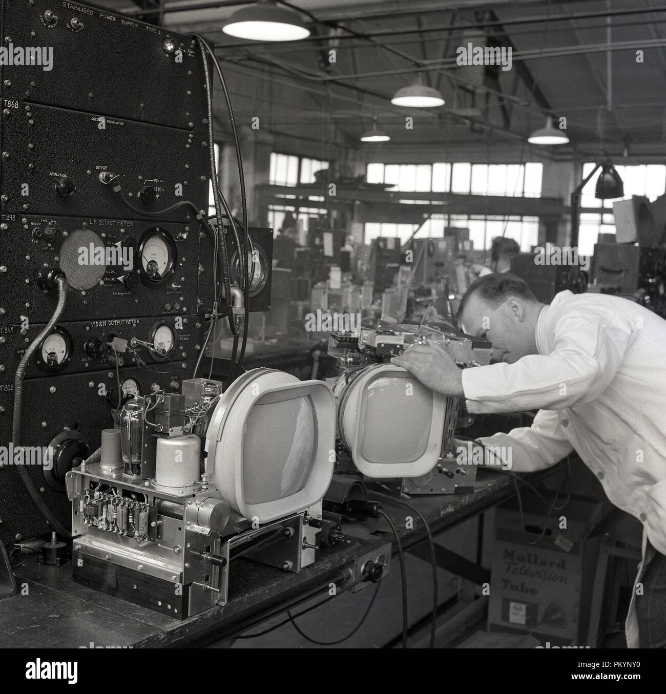1950 s, historischen, weiß beschichteten männlichen Techniker auf den Komponenten der Fernsehgeräte in der Fabrik von Bush Radio, einem führenden britischen consumer electronics Unternehmen in dieser Zeit zu arbeiten. Stockfoto