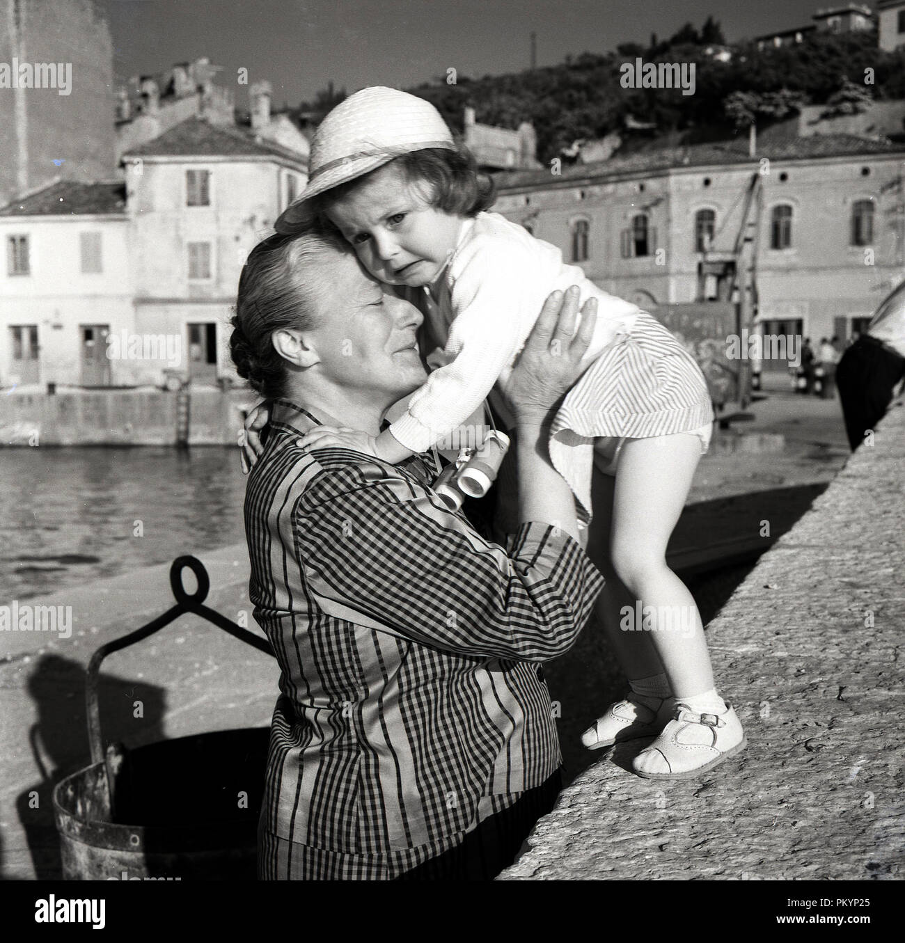 1950, historische, durch einen kleinen Hafen, eine Großmutter hält und Komfort einen aufgeregten kleinen Mädchen, dachte, sie verloren war, Italien. Stockfoto