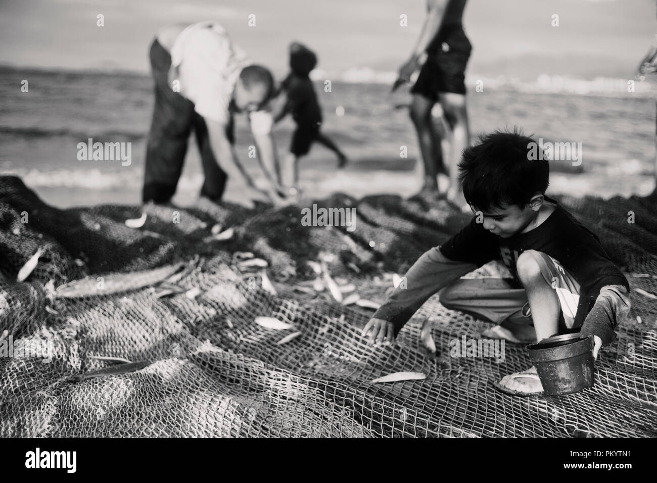 Kind sammelt Fisch im Netz und stellt sie in einen kleinen Eimer. Retro Style Schwarz/Weiß-Fotografie Stockfoto