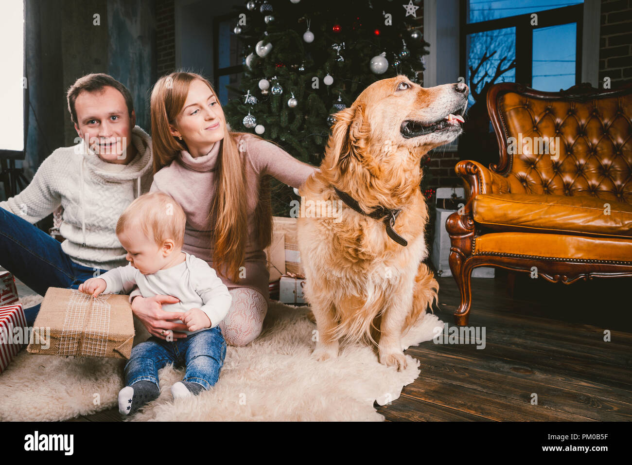 Thema Weihnachten und Neues Jahr Familie Kreis- und Haustier. Mama, Papa und Kind 1 Jahr alt kaukasische Frau sitzt auf dem Boden in der Nähe der Weihnachtsbaum mit Gi Stockfoto