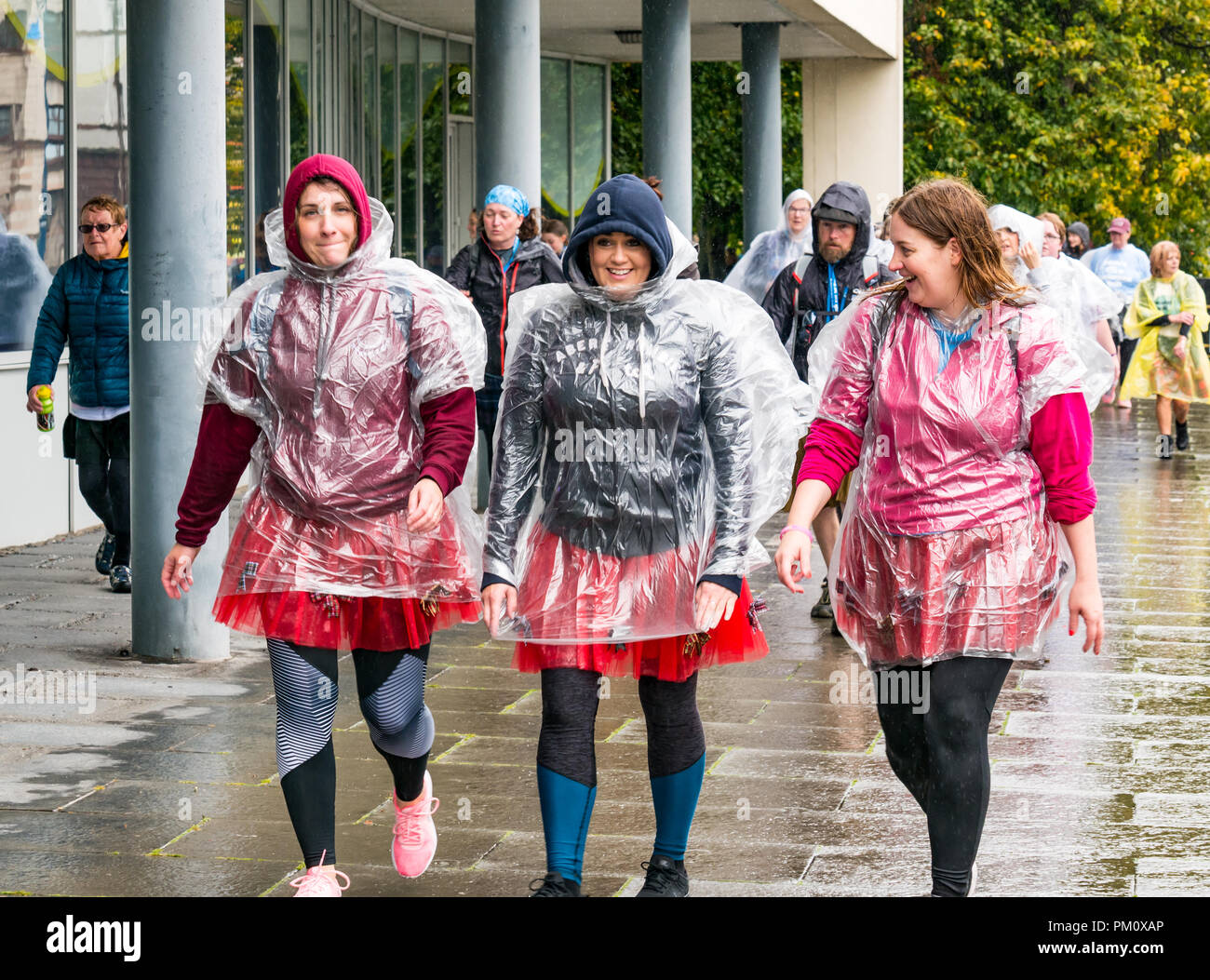Leith, Edinburgh, Schottland, Großbritannien, 16. September 2018. Edinburgh Kilt Walk, gesponsert von der Royal Bank of Scotland, findet heute statt. Wanderer sammeln Mittel für eine Wohltätigkeitsorganisation ihrer Wahl. Die Kilt-Wanderer erreichen die Küste bei etwa 14 km im Regen. Eine Gruppe von Frauen in Kilts und Regen Ponchos Stockfoto