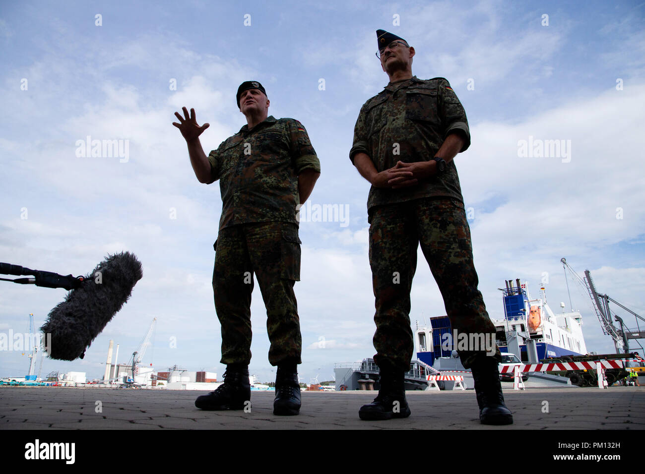 Emden, Deutschland. 16. September 2018. Thomas Hambach (R), Brigadegeneral der Deutschen Luftwaffe, und Ullrich Spannuth, Brigadegeneral der Bundeswehr der Panzerlehrbrigade 9, stehend auf dem Gelände der Emden Habor und sprechen mit Vertretern der Medien, während im Hintergrund die Fahrzeuge der Bundeswehr in ein Ro-ro-Schiff geladen werden. Die NATO-Übung "Trident Zeitpunkt 2018 (TRJE 18)" in Norwegen findet vom 25. Oktober bis 7. November statt. Die Bundeswehr ist fast 10.000 Soldaten und mehr als 4.000 Fahrzeuge nach Norwegen zu übertragen. Ein Schiff wird mit rund 300 Fahrzeuge und Behälter geladen Stockfoto