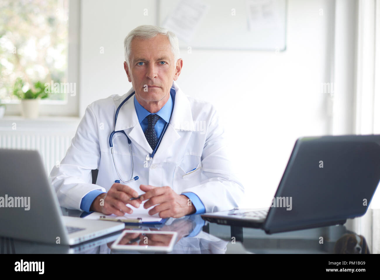 Portrait von älteren männlichen Arzt sitzen an Arztpraxis und Arbeiten am Laptop. Stockfoto