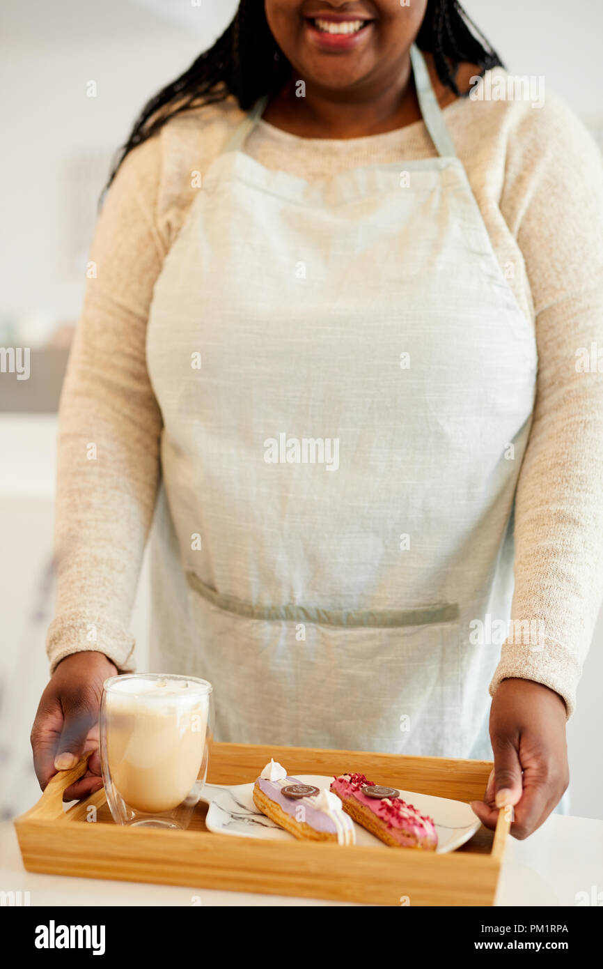 Fröhliche junge Kellnerin in weißen Schürze, Holz- Fach mit Glas Milchshake und zwei leckere Kuchen für einen Kunden Stockfoto