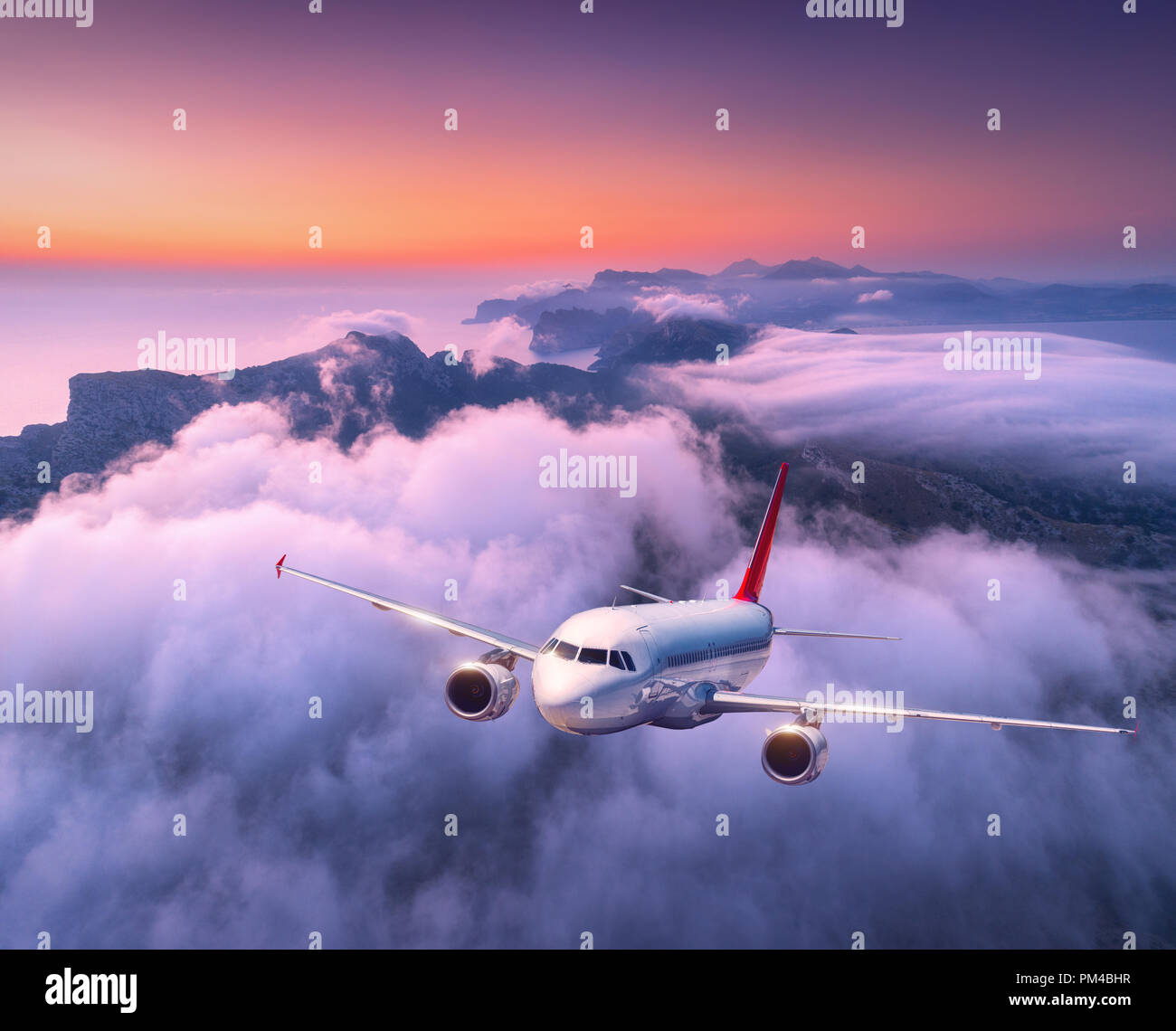 Pkw Flugzeug über Wolken bei Sonnenuntergang fliegen. Landschaft mit großen weißen Flugzeug, niedrige Wolken, Meer, purple sky in der Abenddämmerung. Flugzeug landet. Geschäft Stockfoto