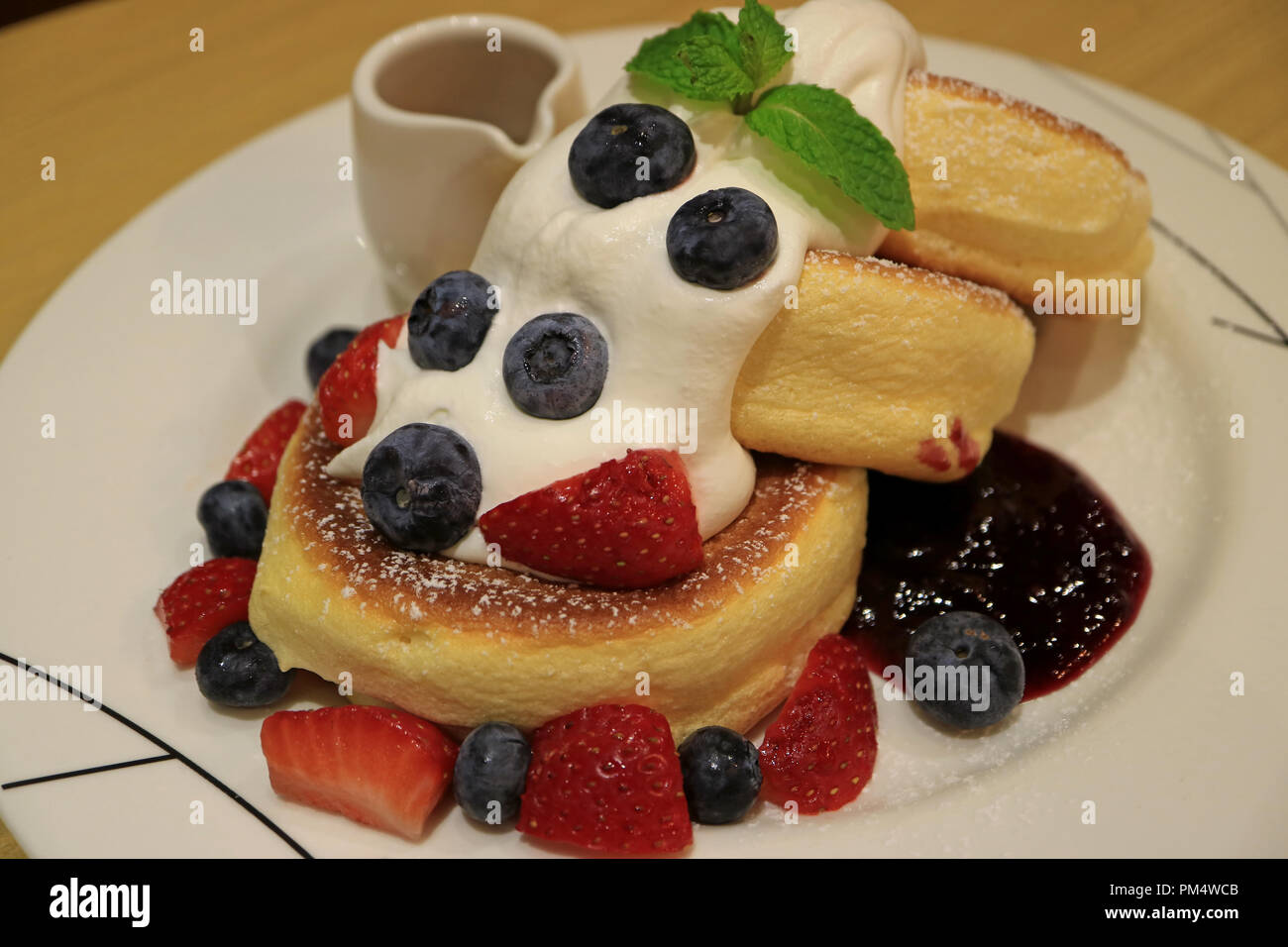 Flauschige Souffle Pfannkuchen mit Beeren Sauce, frische Sahne und Mix Beeren serviert auf weiße Platte Stockfoto