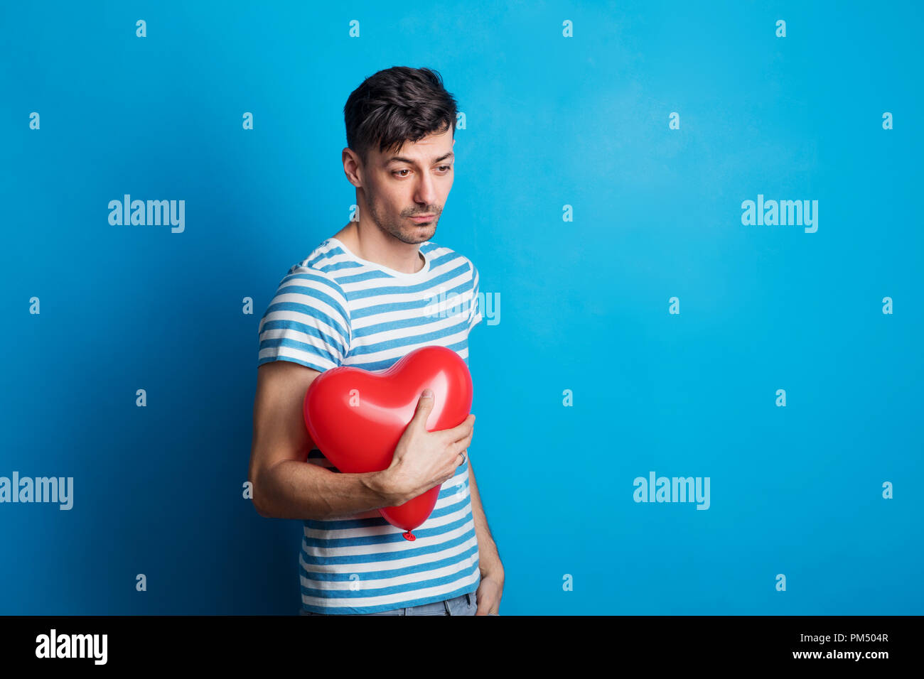 Porträt der traurige junge Mann im Studio auf einem blauen Hintergrund, mit roten Herzen. Stockfoto