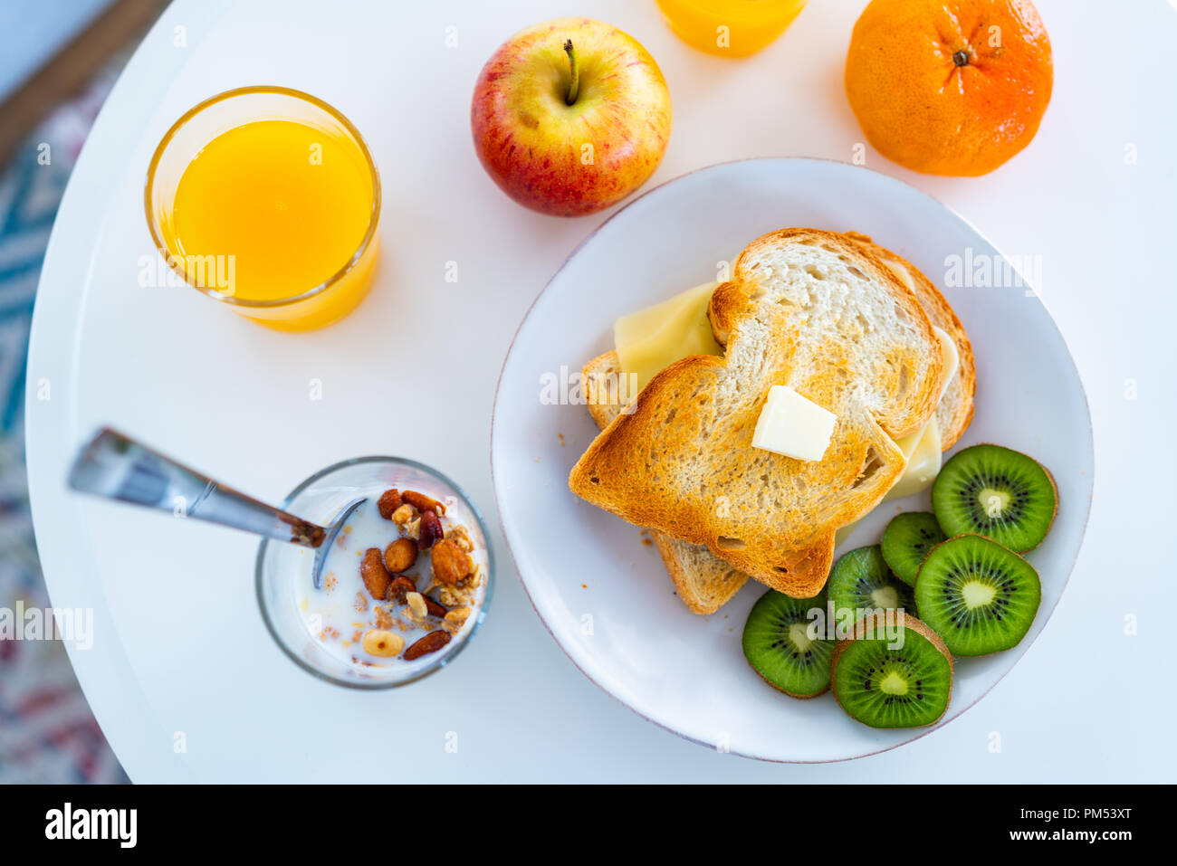 Komplettes Frühstück mit Apfel, Orange, clemente, Obst, Orangensaft, Milch und Müsli in eine Tasse, geröstetes Brot mit Butter und Käse, in Scheiben geschnitten und Kiwi. Stockfoto