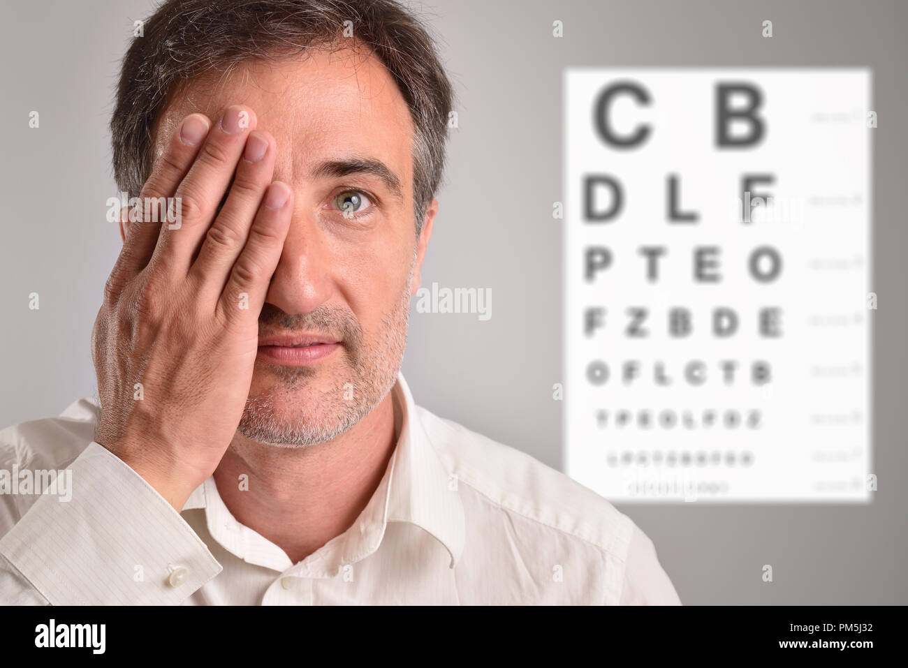 Mann im mittleren Alter, die ein Auge für die optische Überarbeitung mit Brief chart im Hintergrund. Horizontale Zusammensetzung Stockfoto