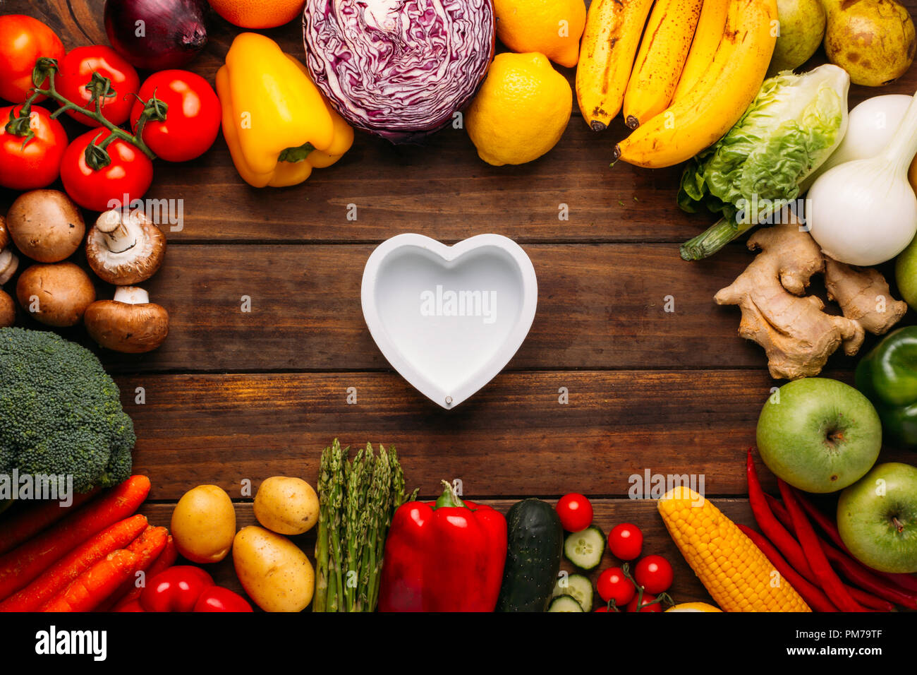 Blick von oben auf einen hölzernen Tisch voller Gemüse und in der Mitte des Bildes eine leere Herzförmige Schale, konzeptionelle Foto, für Gourmets Stockfoto