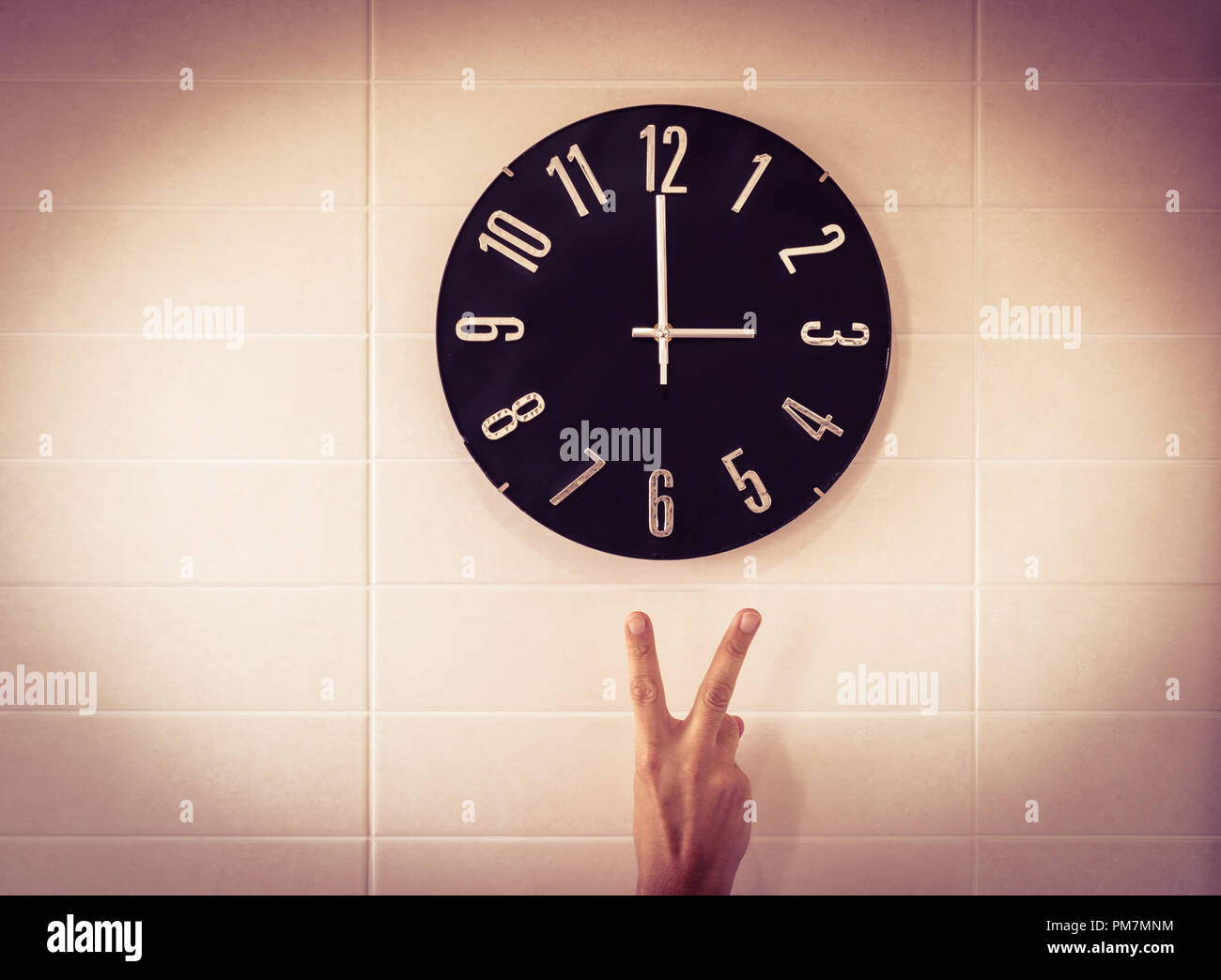 Große schwarze Uhr auf weiße Wand. Zeit ändern. DST. Erhebung der Europäischen Union zu der Zeit ändern. Geste der Sieg. Kaukasische Mann. Stockfoto