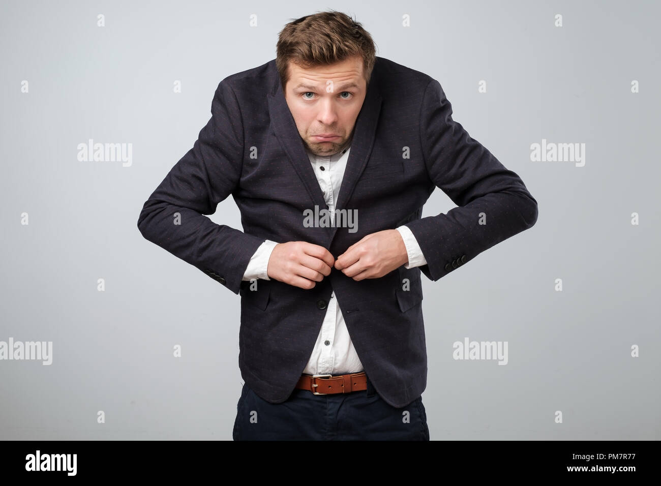 Nicht in das Konzept. Junge ungepflegte Mann in großen Anzug versuchen, einen Knopf zu befestigen. Er ist nervös und gestresst. Stockfoto