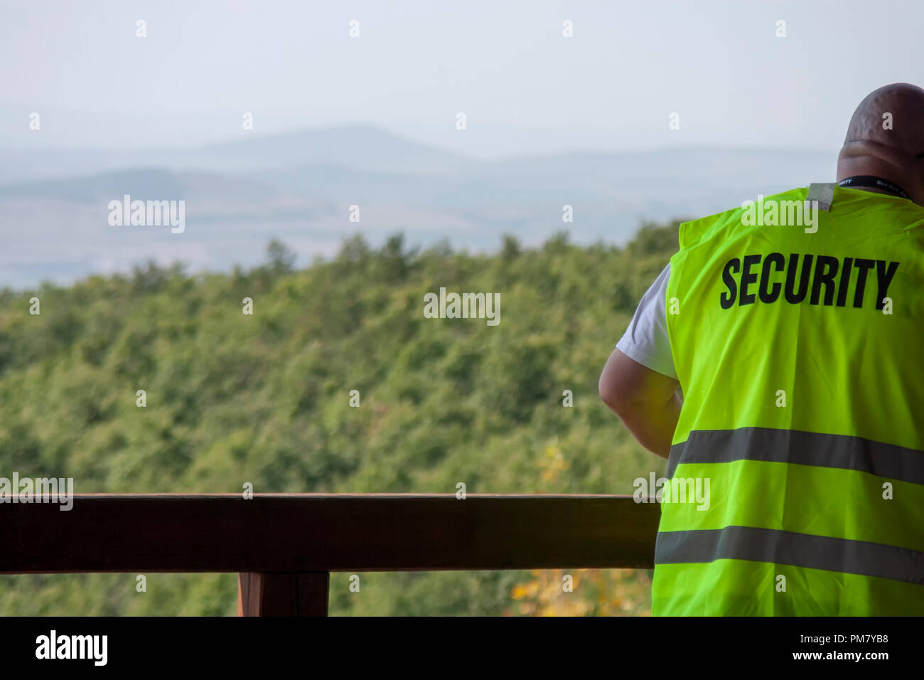 Security Guard in gelb Weste neben dem Geländer mit schönen Wald auf die Landschaft im Hintergrund. Copyspace. Stockfoto