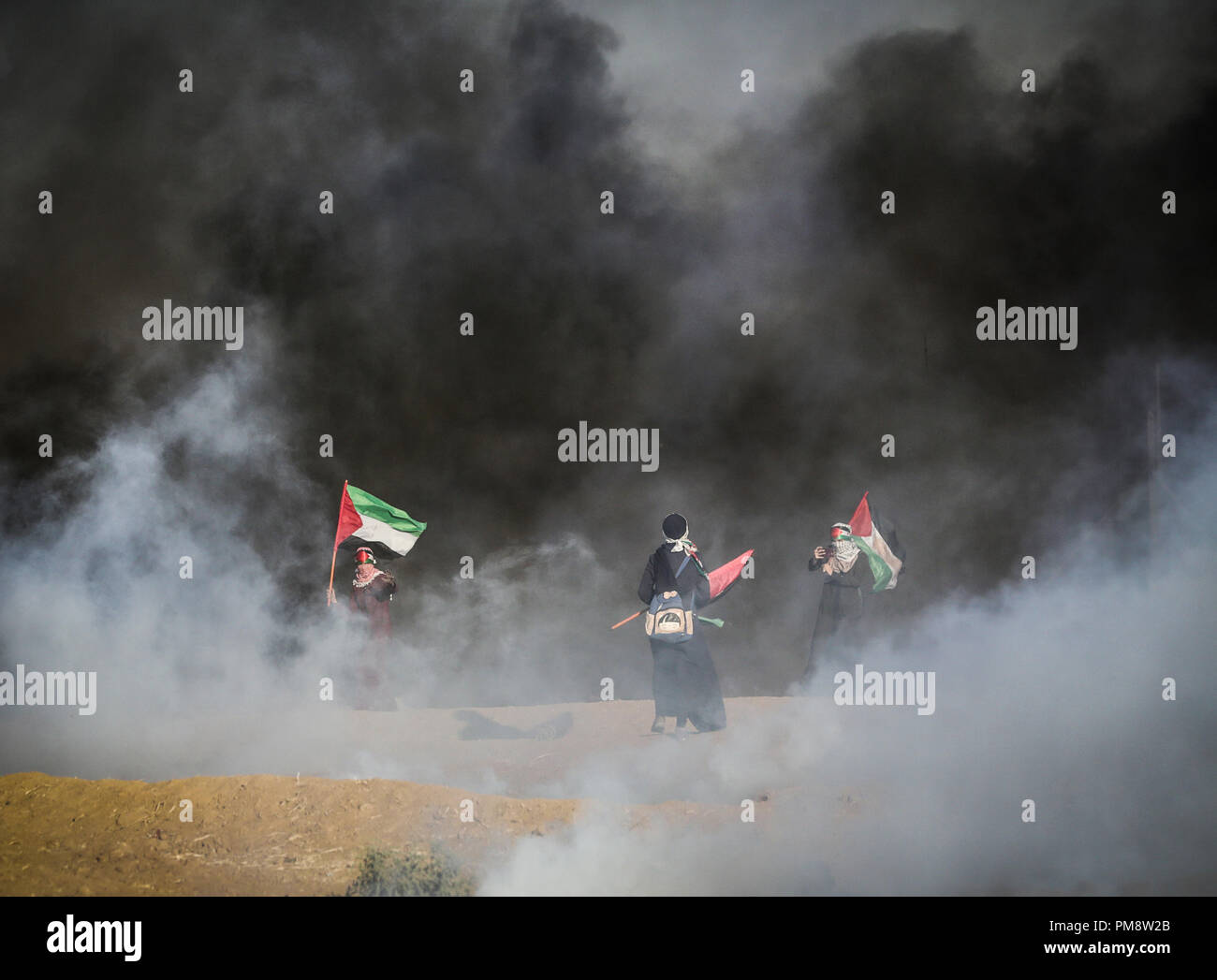 Palästinensische Frauen gesehen Holding flags zwischen riesigen rauchwolken während der Auseinandersetzungen. Auseinandersetzungen zwischen palästinensischen Demonstranten und israelischen Kräfte während eines Protestes entlang der israelischen Zaun östlich von Gaza-stadt. Stockfoto