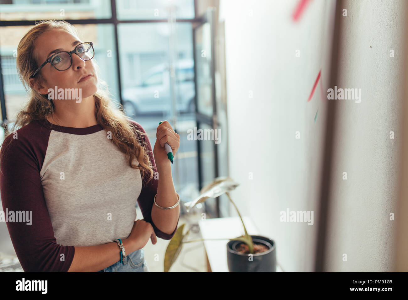 Junge Frau, die in Büro- und Blick auf die Schautafel denken. Weibliche Programmierer denken über neue Projekt Plan am tech Start Stockfoto
