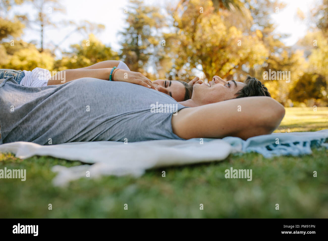 Paar entspannende in einem Park liegen auf dem Boden und Reden. Frau schlafen auf Arm von ihrem Freund in einem Park an einem sonnigen Tag. Stockfoto