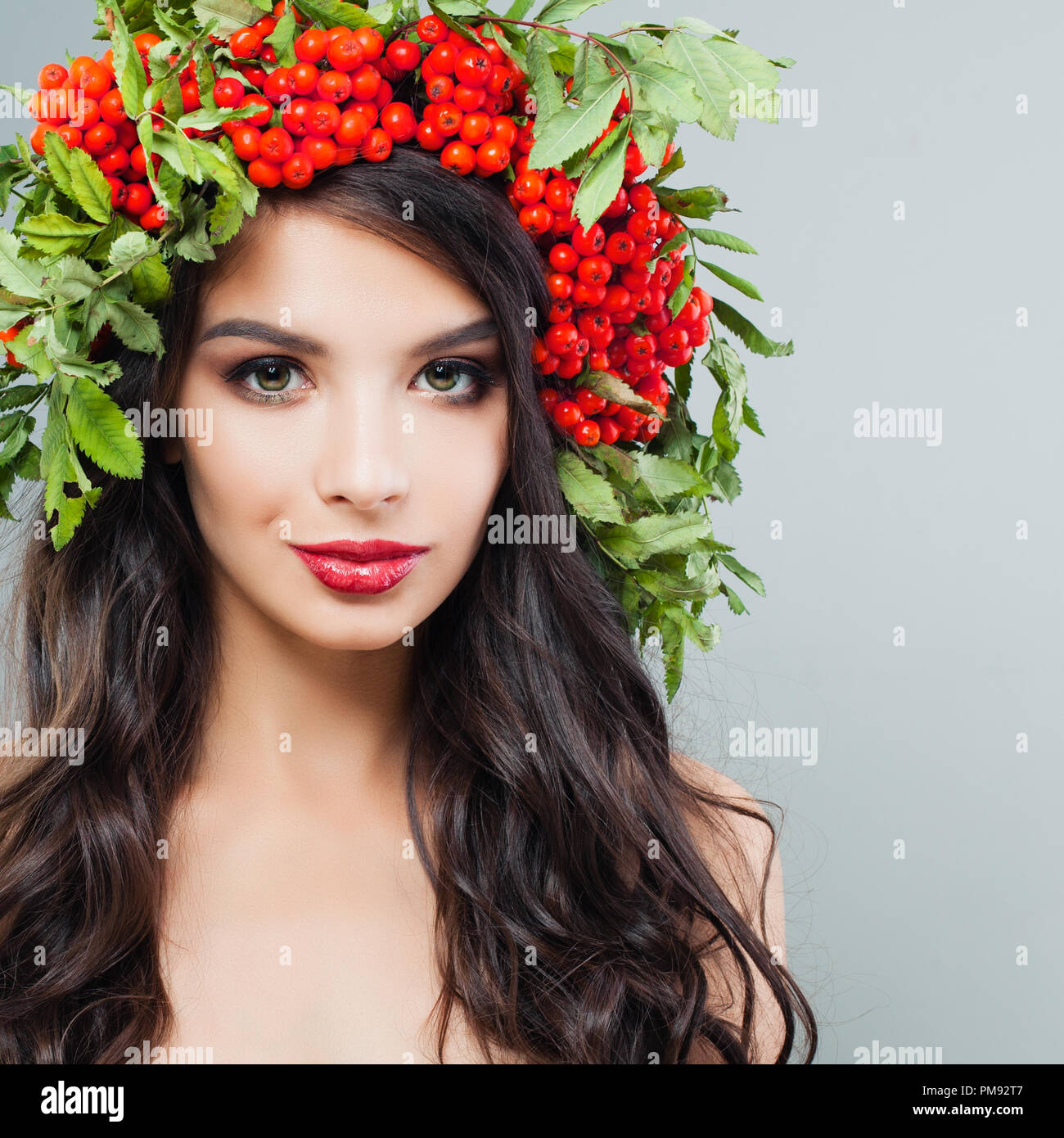 Junge Frau Gesicht. Brunette weibliche Modell mit Langen lockigen Frisur und roten Beeren und grüne Blätter auf dem Kopf Stockfoto