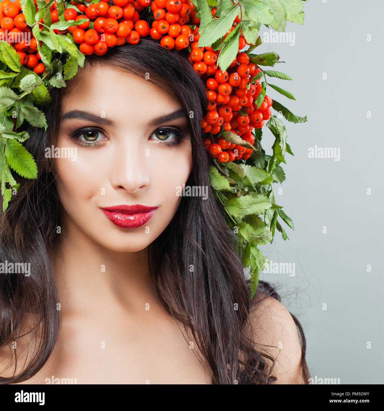 Fröhliche junge Frau Brünette mit roten Lippen Make-up, lange wellige Haare und Vogelbeeren und Blätter Kranz Stockfoto