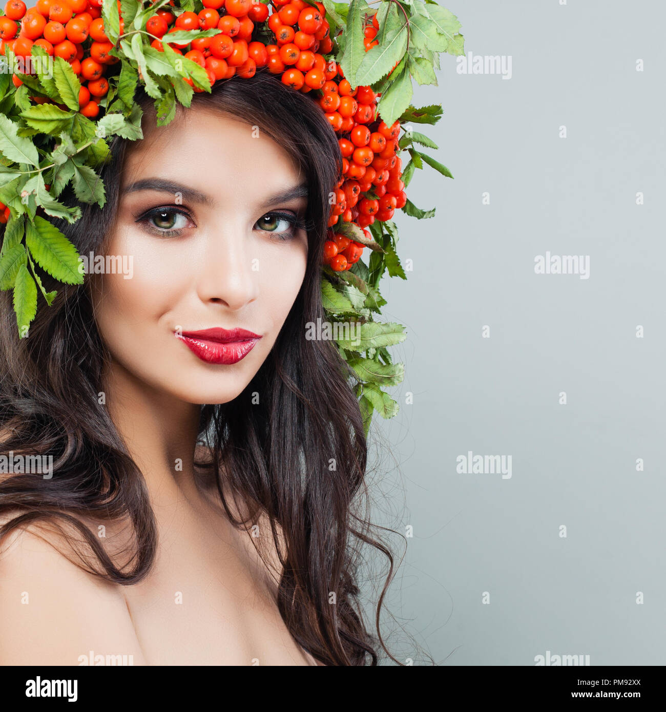 Pretty Woman Brünette mit roten Lippen Make-up, lange wellige Haare und Vogelbeeren und hinterlässt auf dem Kopf Stockfoto