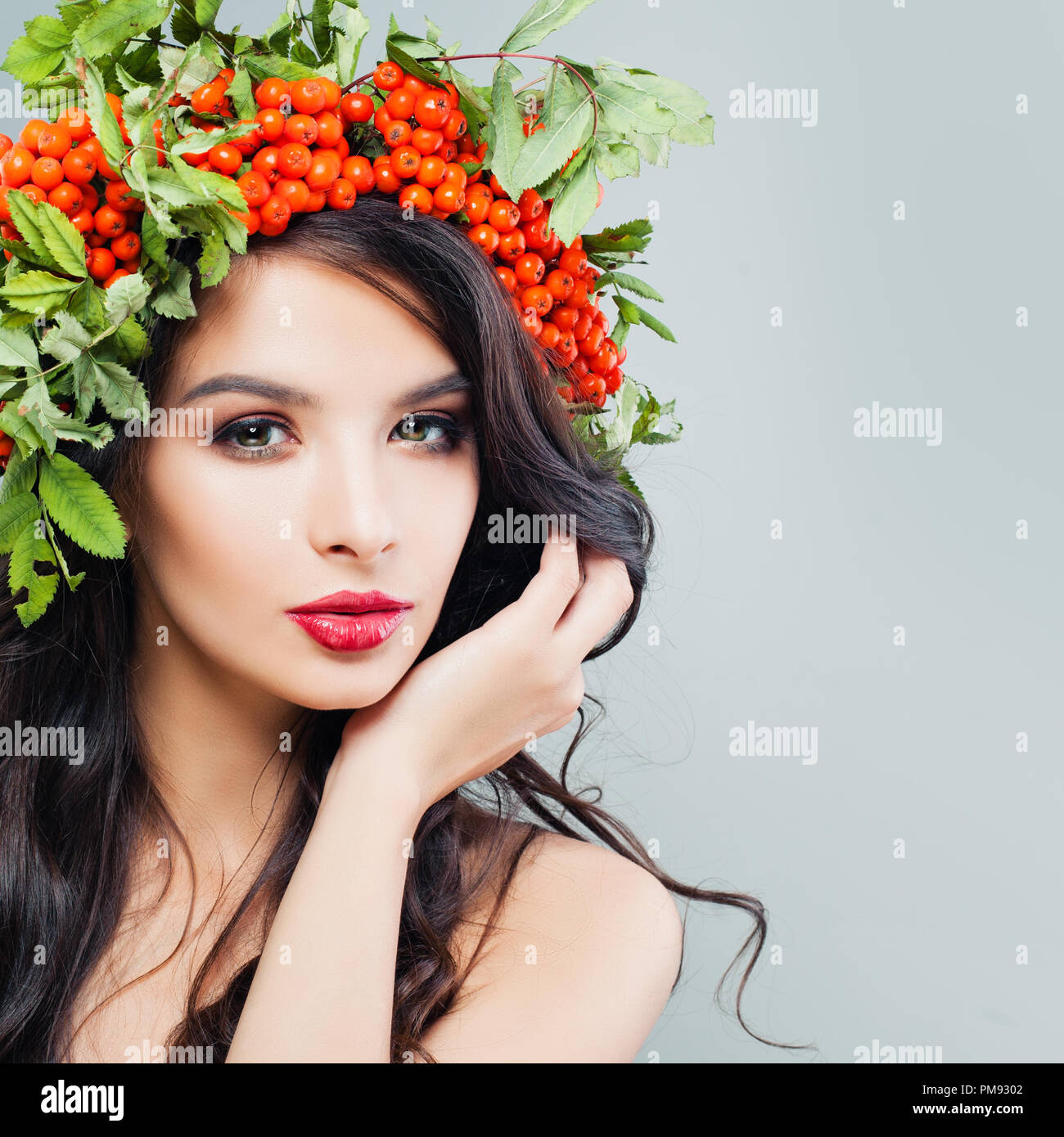 Natürliche Schönheit. Junge Frau mit Make-up-niedlich, lange wellige Haare und rote Beeren und grüne Blätter auf dem Kopf Stockfoto