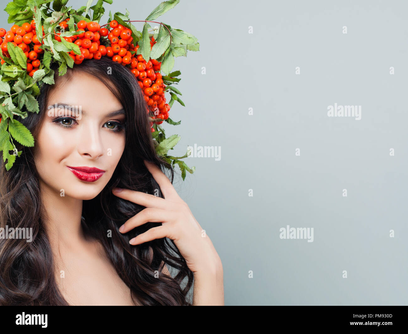 Junge Frau lächelnd. Brunette Mädchen mit Make-up, gesunde gewelltes Haar, roten Beeren und grüne Blätter auf Hintergrund mit Kopie Raum Stockfoto
