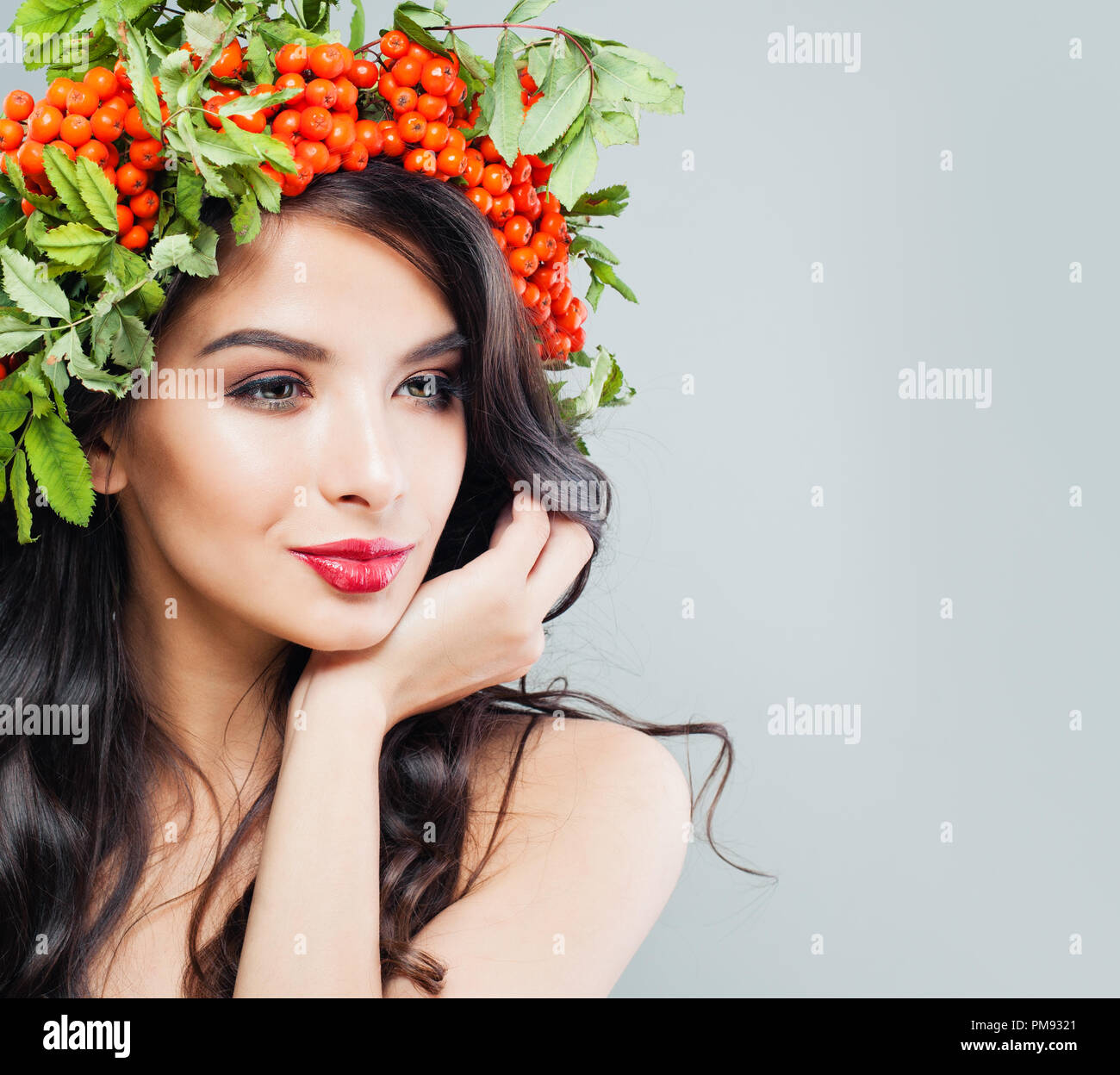 Perfekte junge brünette Frau mit langen gewelltes Haar, Make-up und roten Beeren und grünen Blättern. Schönen weiblichen Gesichts Stockfoto