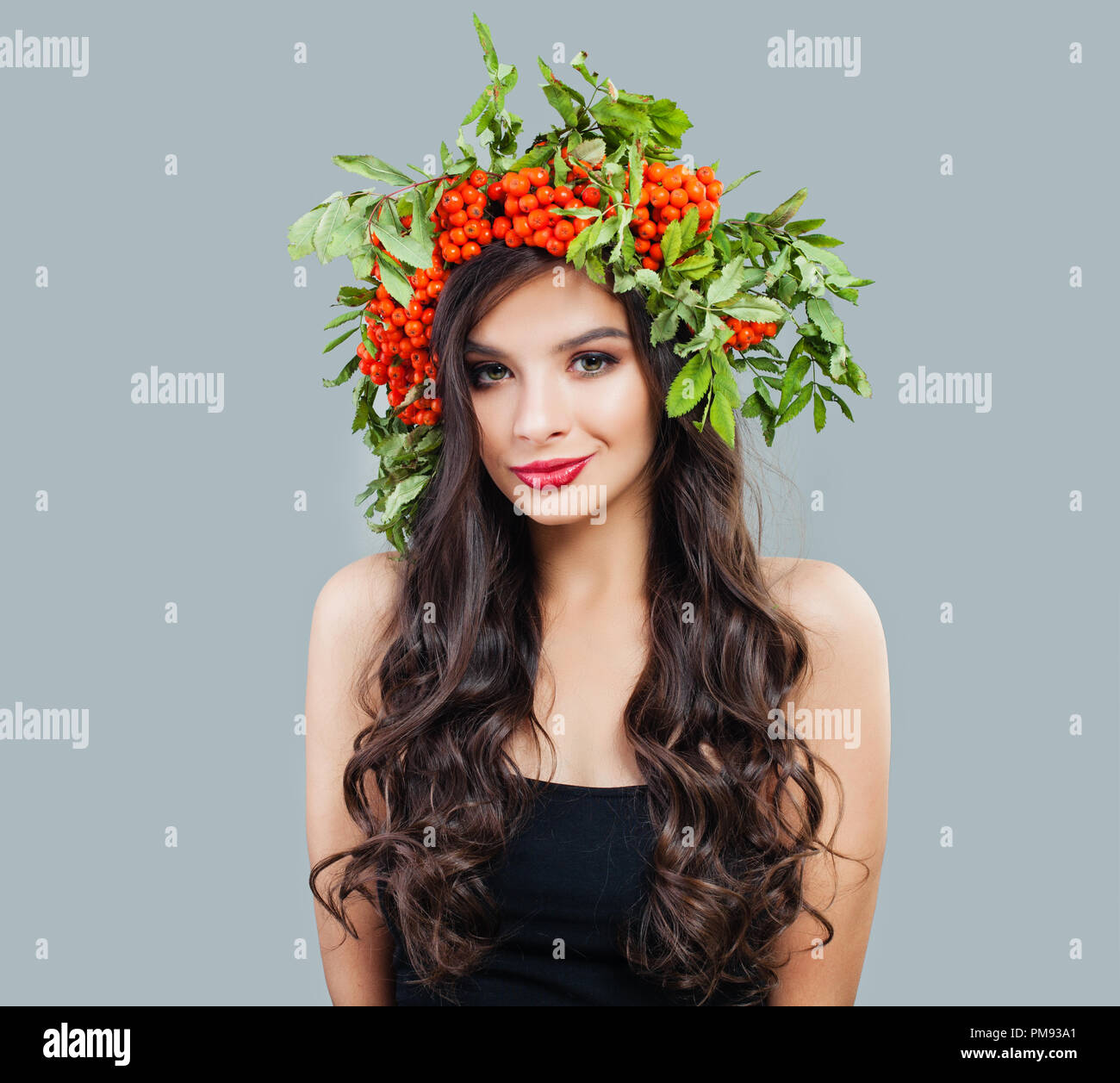 Schöne brünette Frau Mode Modell mit gesunden curly Frisur, Make-up und roten Beeren und grüne Blätter, Porträt Stockfoto