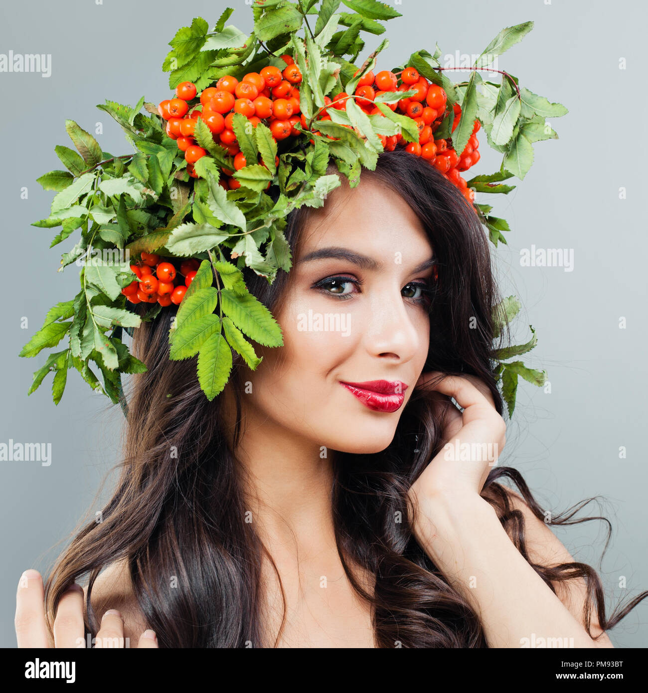 Porträt der jungen Frau mit Make-up, welliges Haar und roten Beeren und grüne Blätter auf dem Kopf Stockfoto