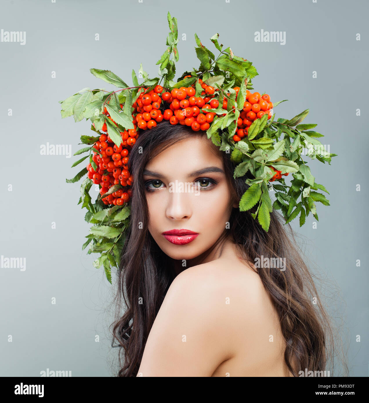 Schöne Frau Mode Modell mit gesunden curly Frisur, Make-up und roten Beeren und grüne Blätter, Porträt Stockfoto