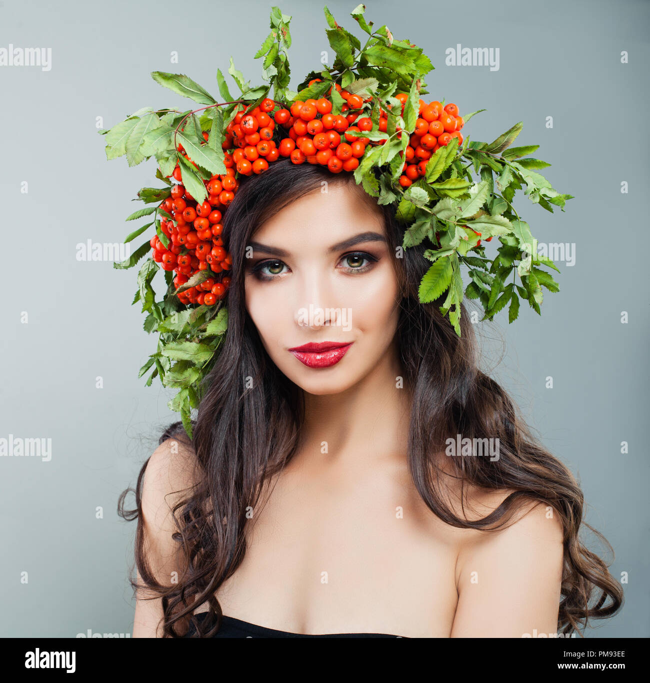 Junge brunette woman fashion Modell mit gesunden curly Frisur, Make-up und roten Beeren und grünen Blättern im Haar Stockfoto