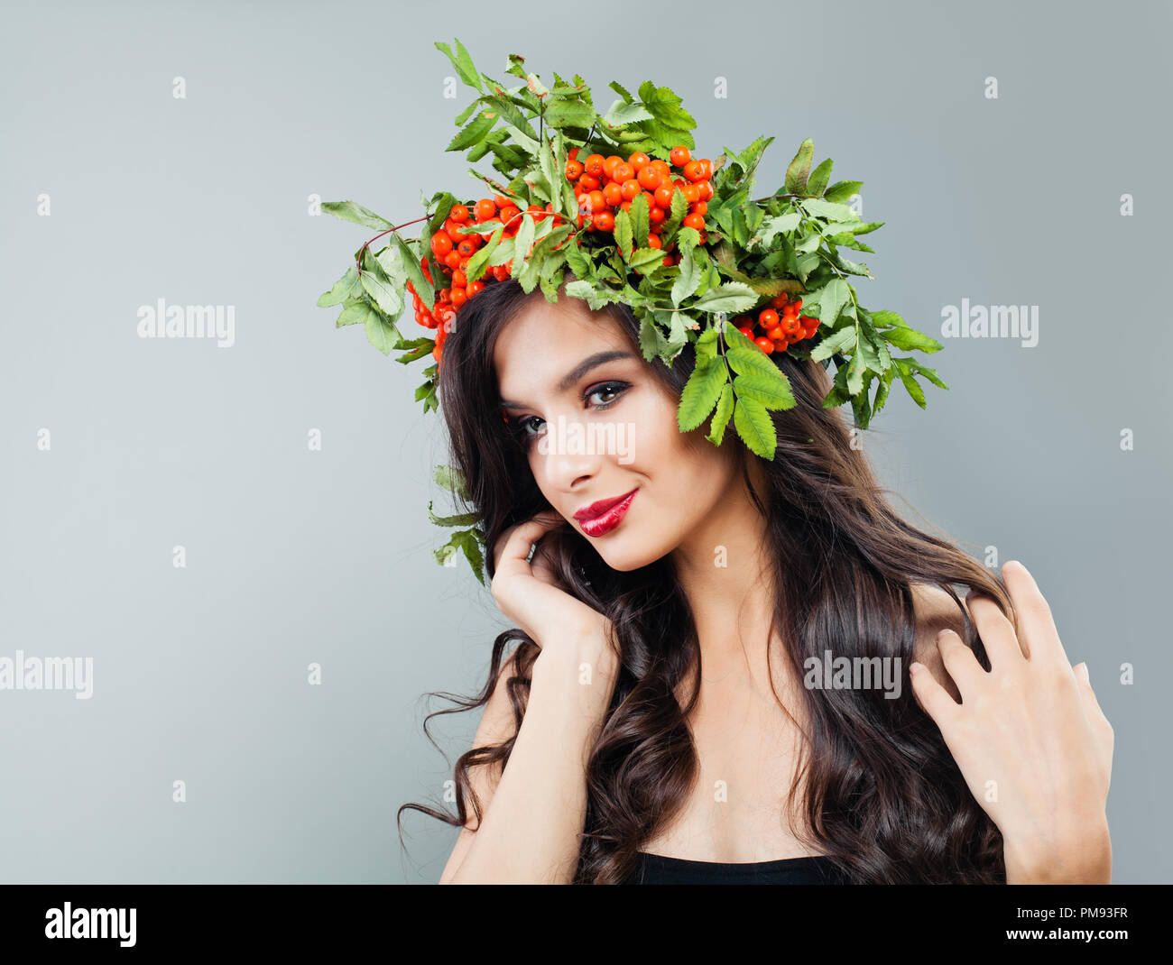 Brünette Schönheit. Junge Frau Mode Modell mit gesunden curly Frisur, Make-up und roten Beeren und grüne Blätter Stockfoto