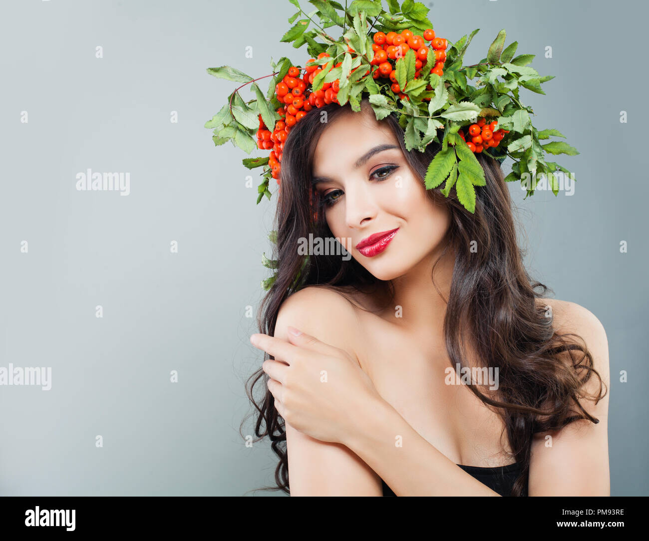 Lächelnde Frau fashion model. Nettes Gesicht, Lächeln, gesunde lockige Haare, Make-up und roten Beeren und grüne Blätter Stockfoto