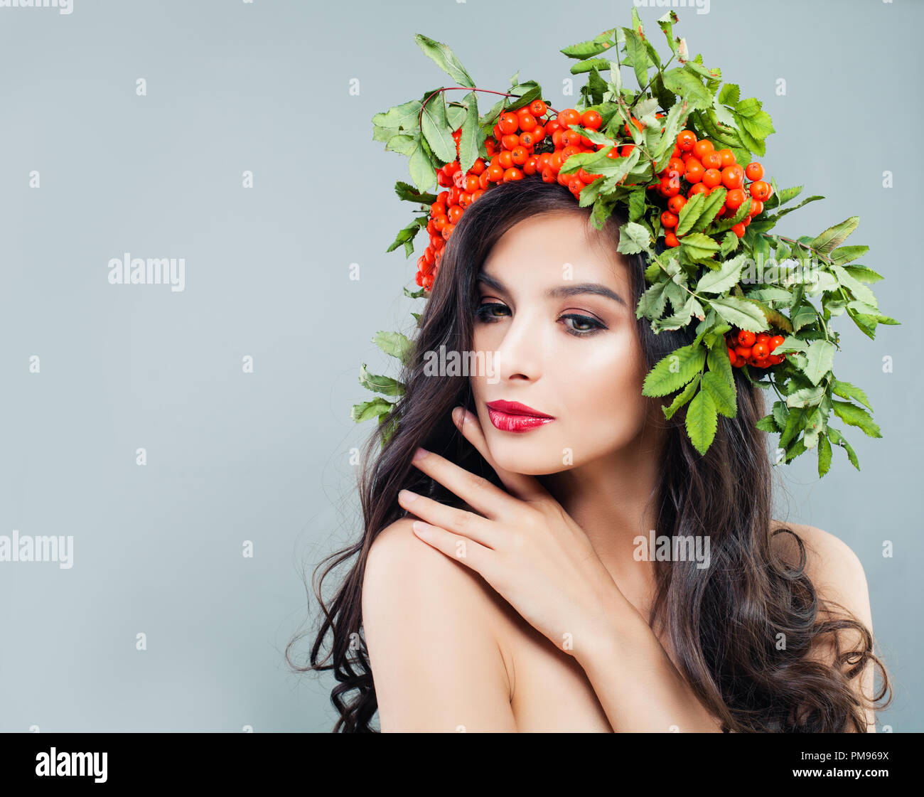 Natürliche Schönheit. Hübsche brünette Frau mit gesunden wellig Frisur, Make-up und roten Beeren und grüne Blätter Stockfoto